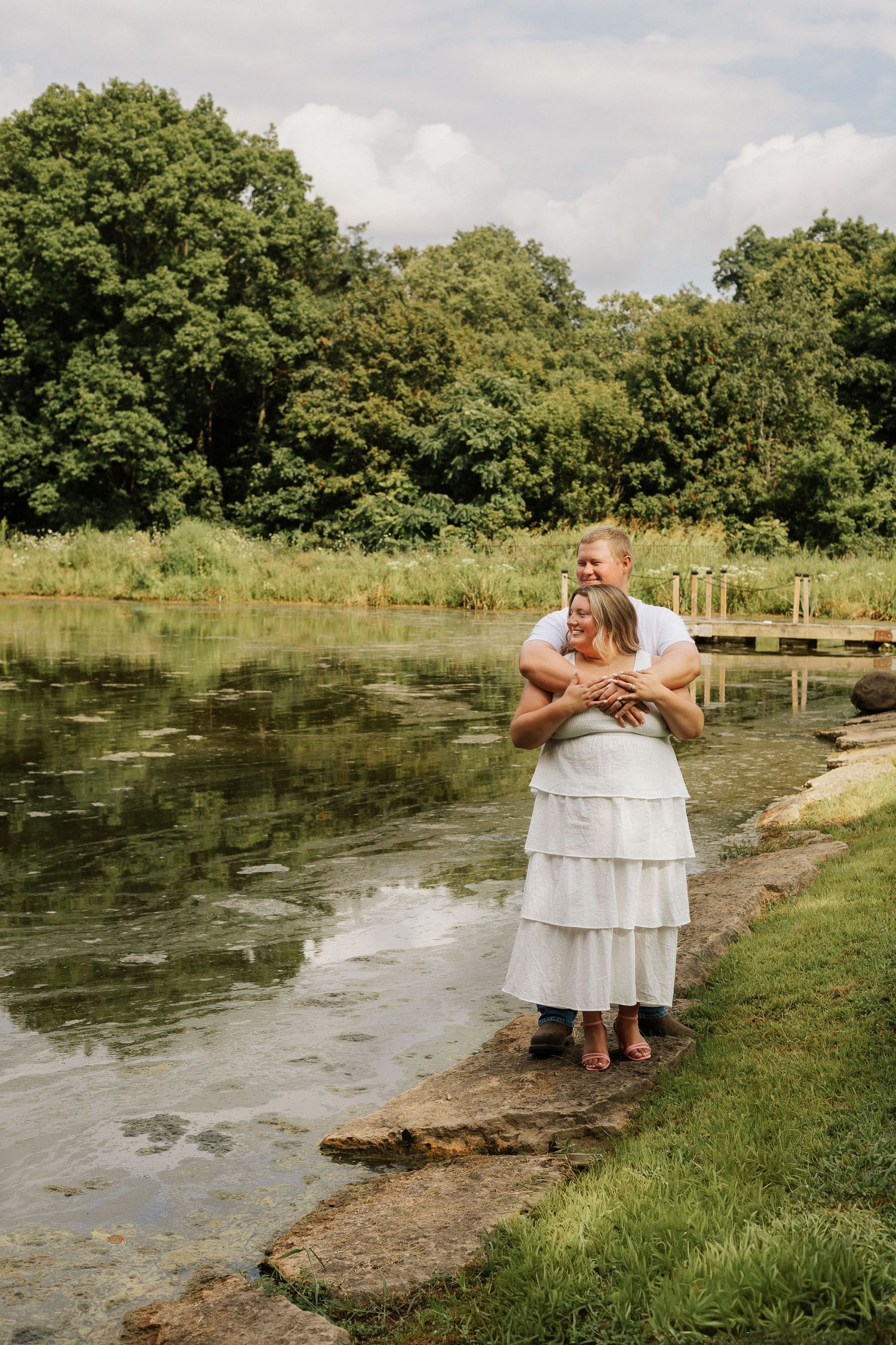 A couple sits by a scenic pond surrounded by lush greenery.