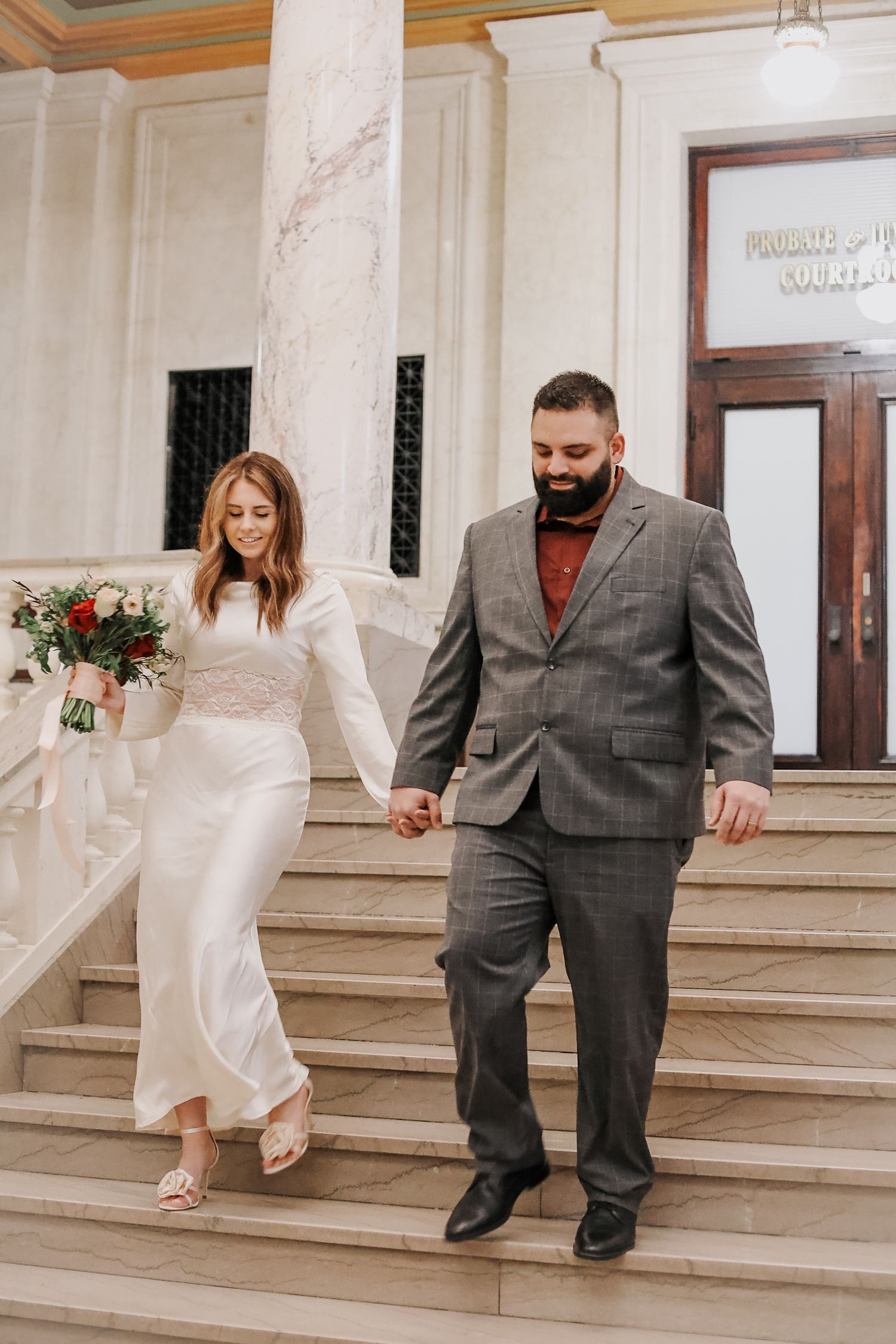 Wedding couple descending marble steps in formal attire.