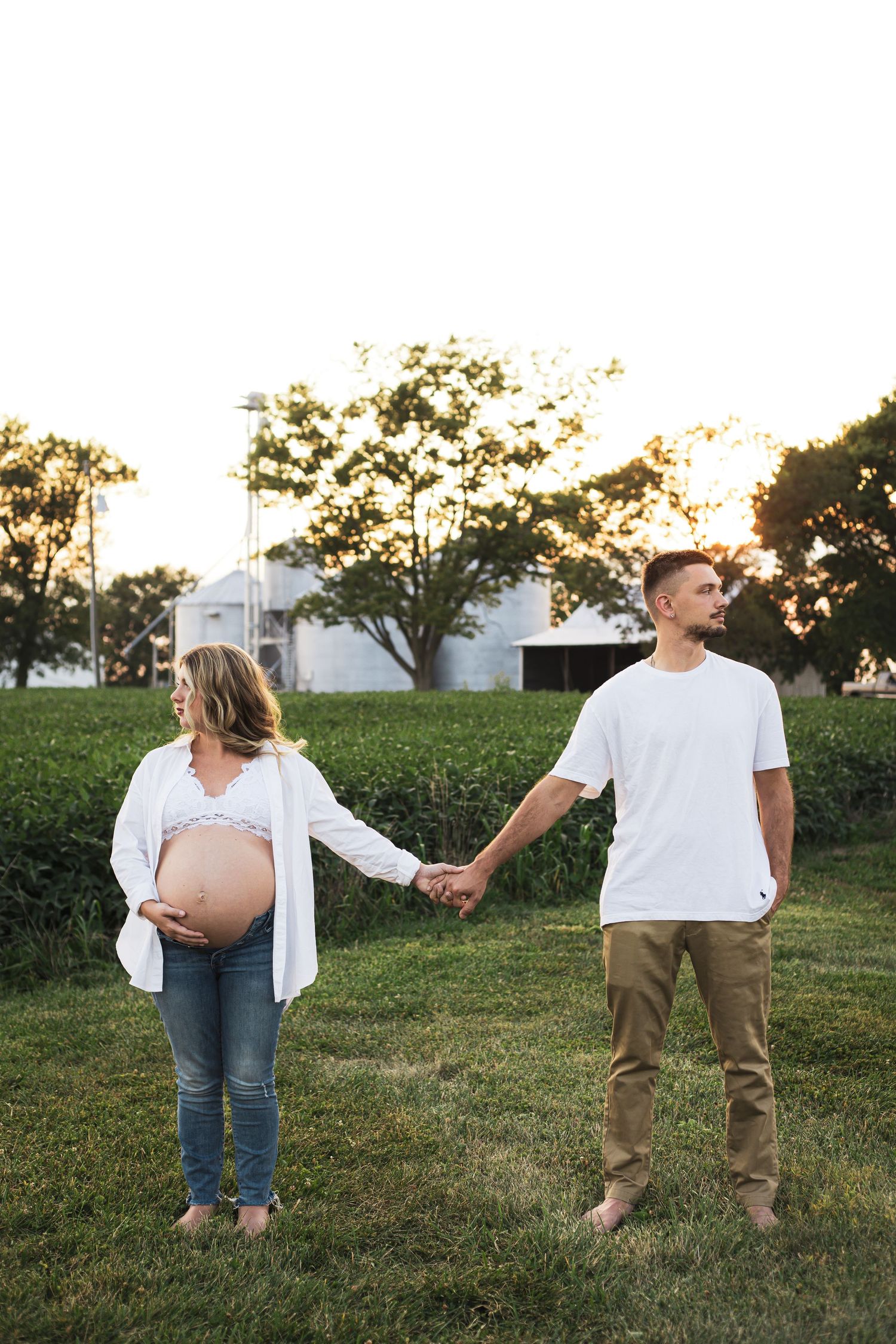 Casual outdoor maternity photos of couple in white and khaki clothing at sunset.
