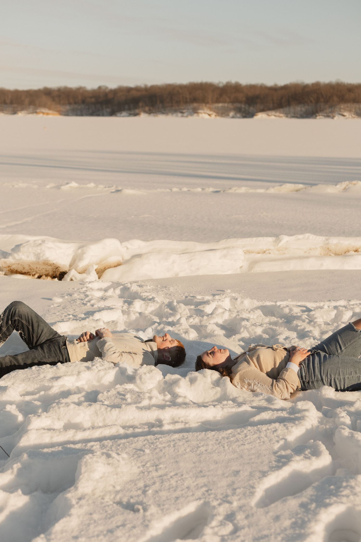 Two people lie back in the snow together during a winter photoshoot.