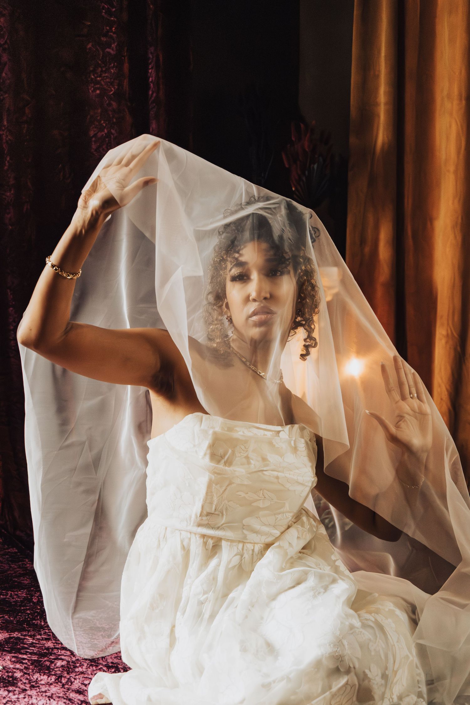 Ethereal bridal portrait through sheer veil with soft lighting and natural curls.