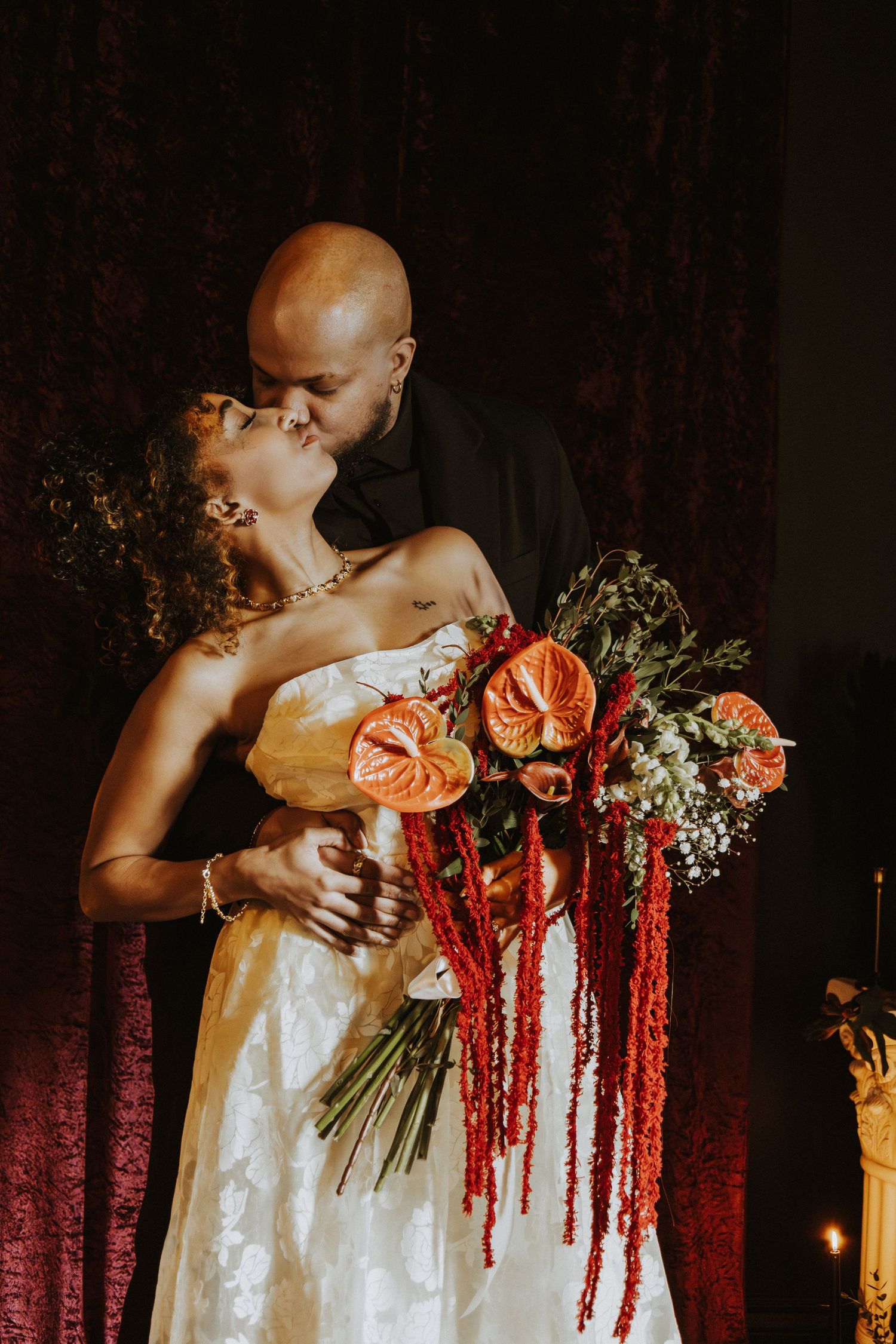 Romantic wedding portrait with stunning red and orange floral bouquet against burgundy curtain.