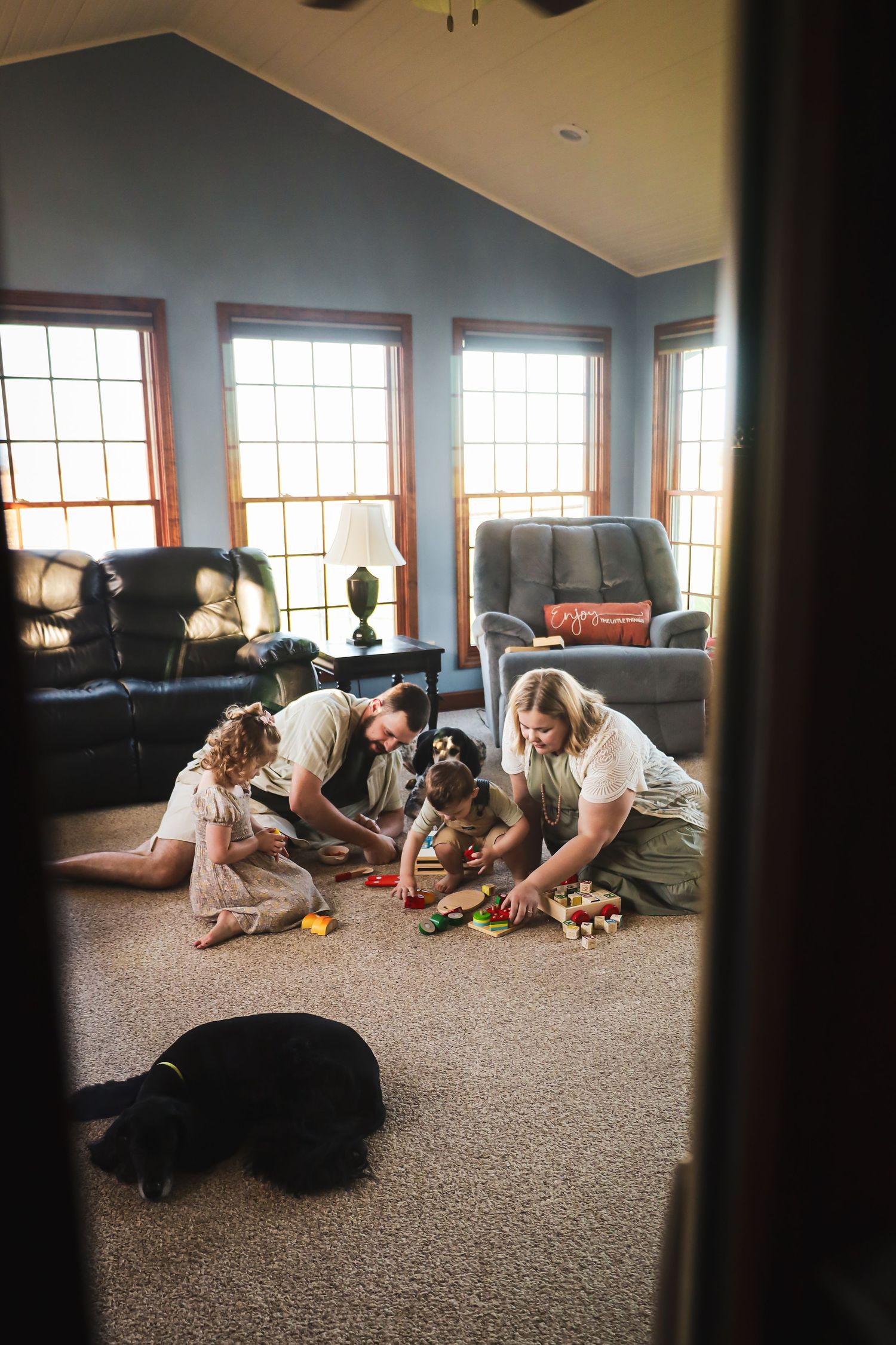 Family playing together on the floor of a sunlit room with large windows.