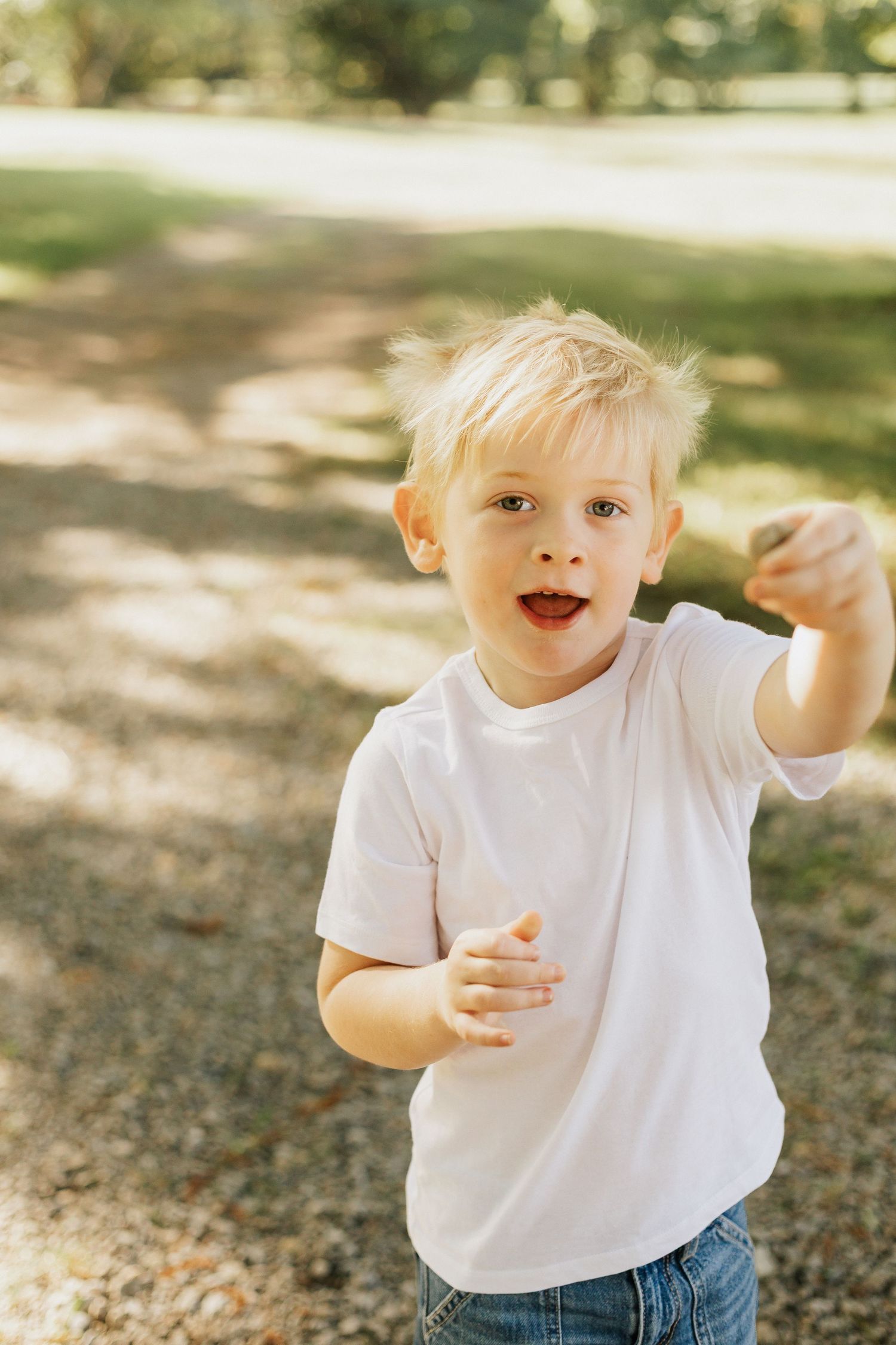Energetic toddler in white t-shirt playing outdoors in dappled sunlight.