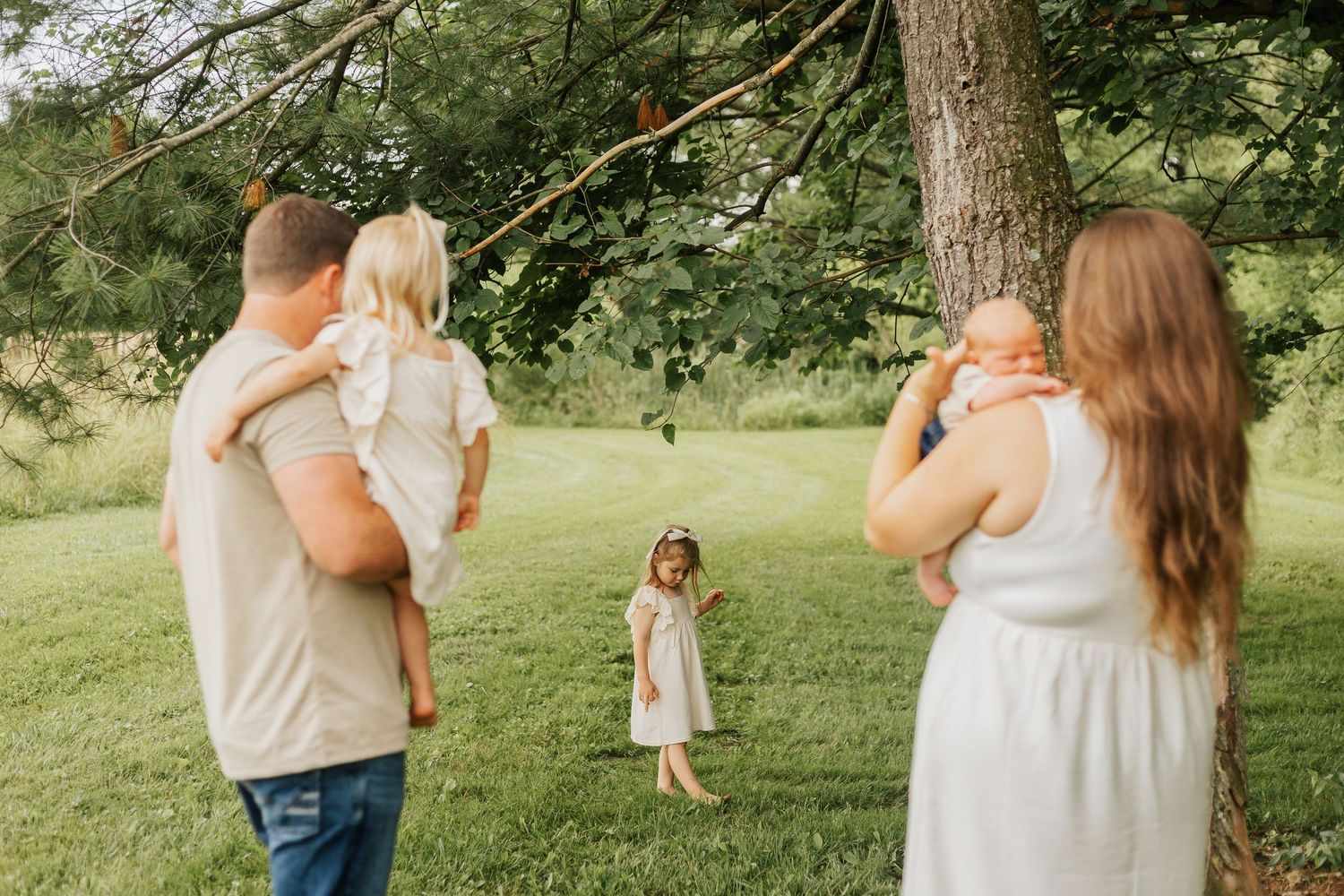 Parents holding children while young girl dances in grassy field.