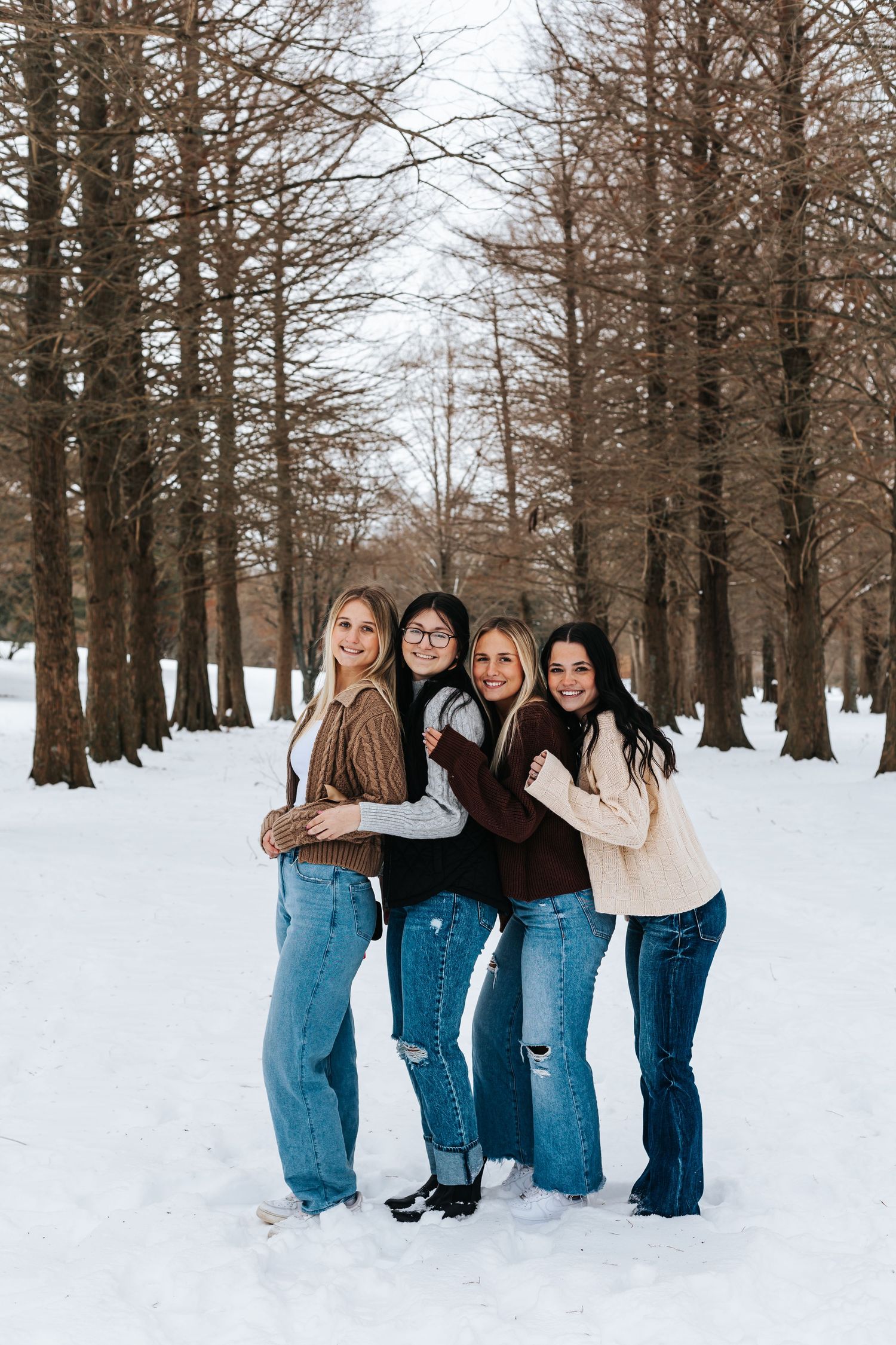 Group of friends wearing matching jeans pose together in snowy winter forest setting.