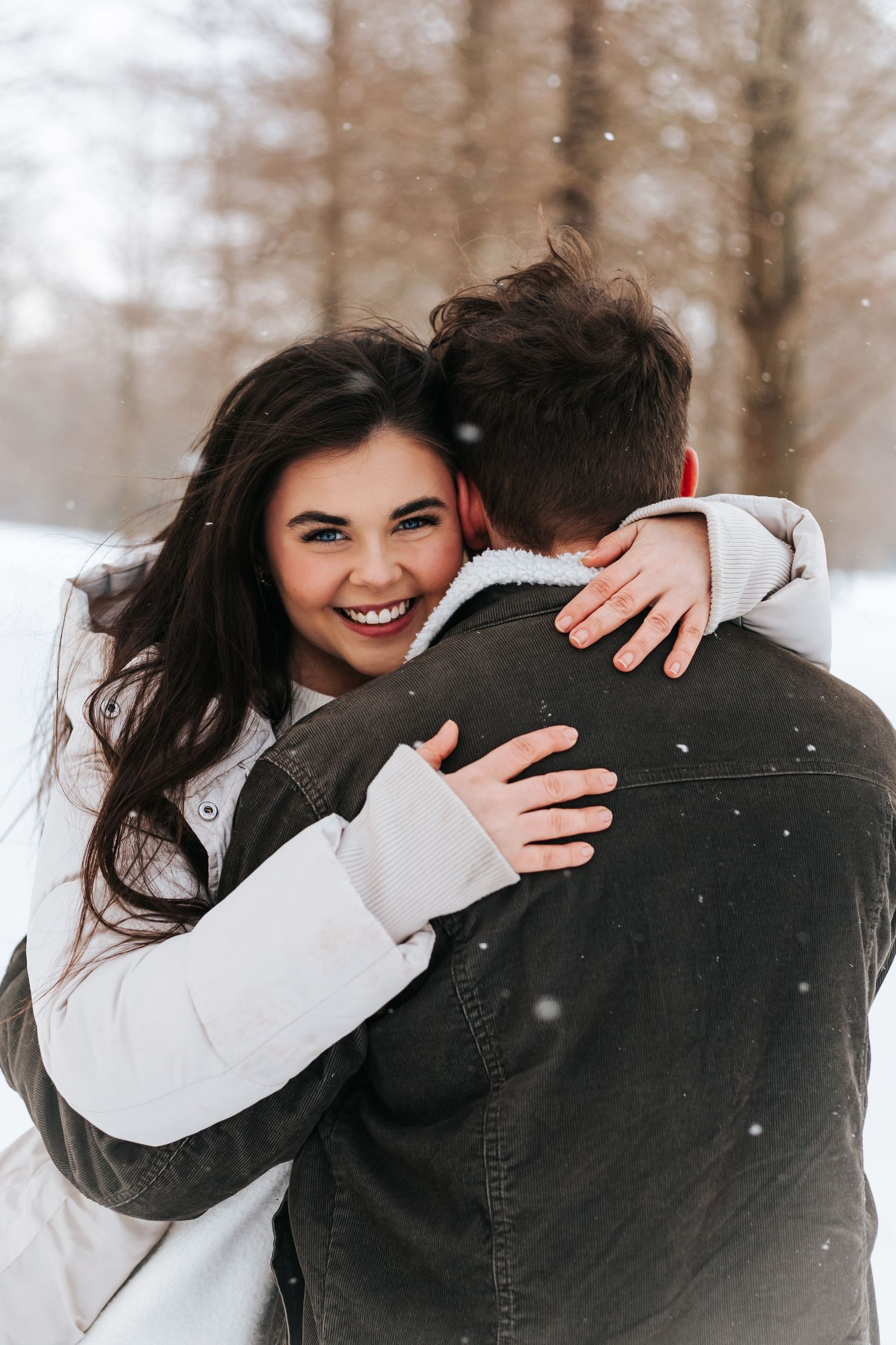 Joyful embrace in winter scene with snow falling and trees in background.