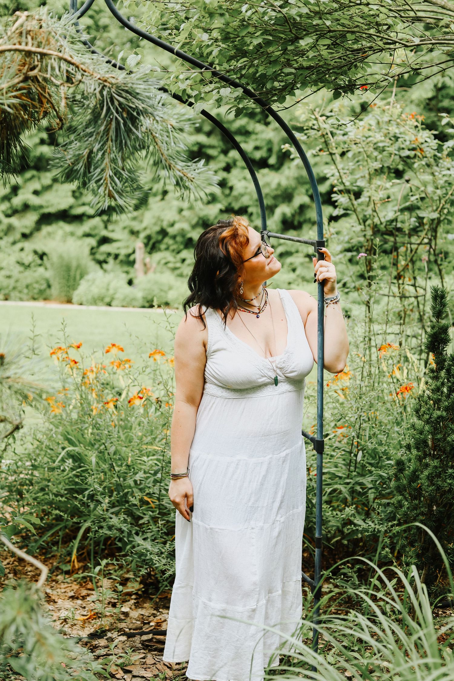 A white sundress stands among vibrant orange flowers and lush garden greenery.