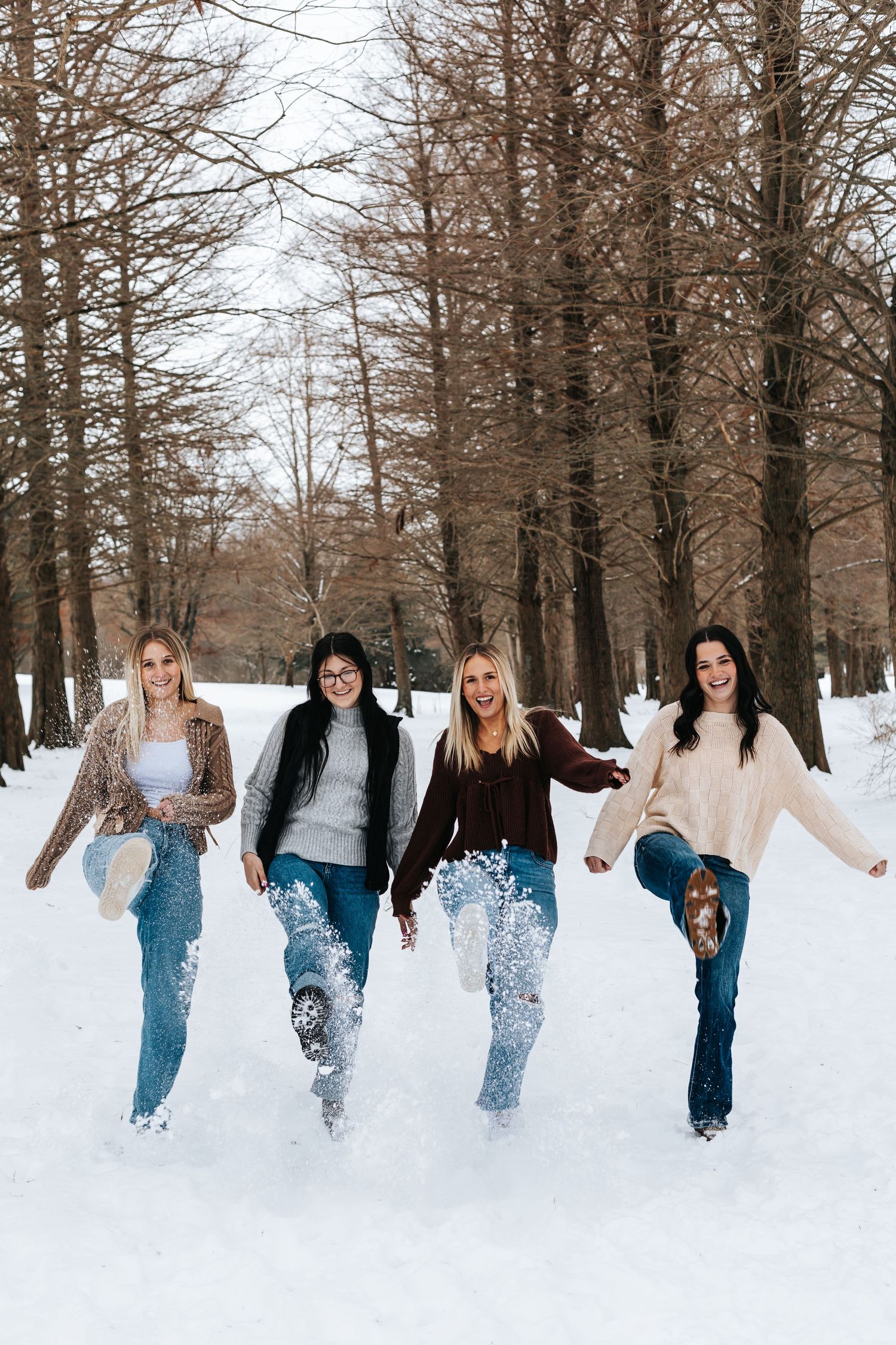 People kicking up snow while running through a winter forest landscape.