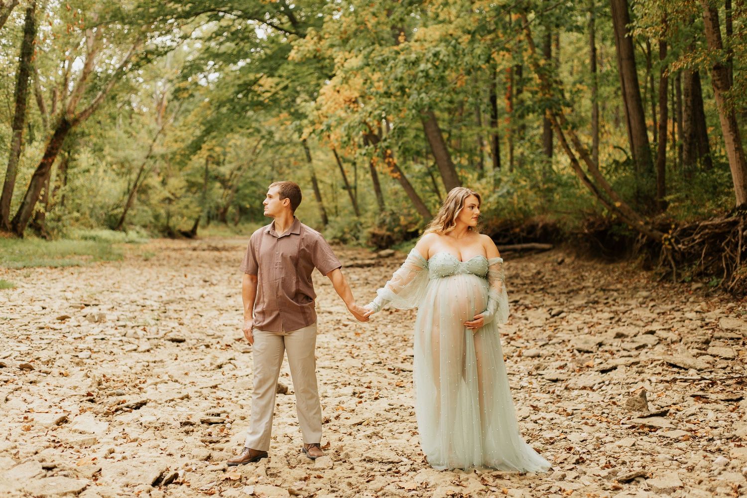 Expecting couple holding hands in romantic forest maternity photo session.