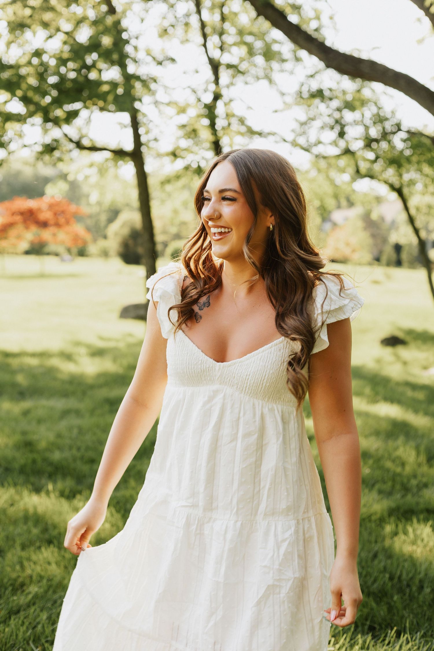 Portrait of a person in white summer dress standing in sunny park setting.
