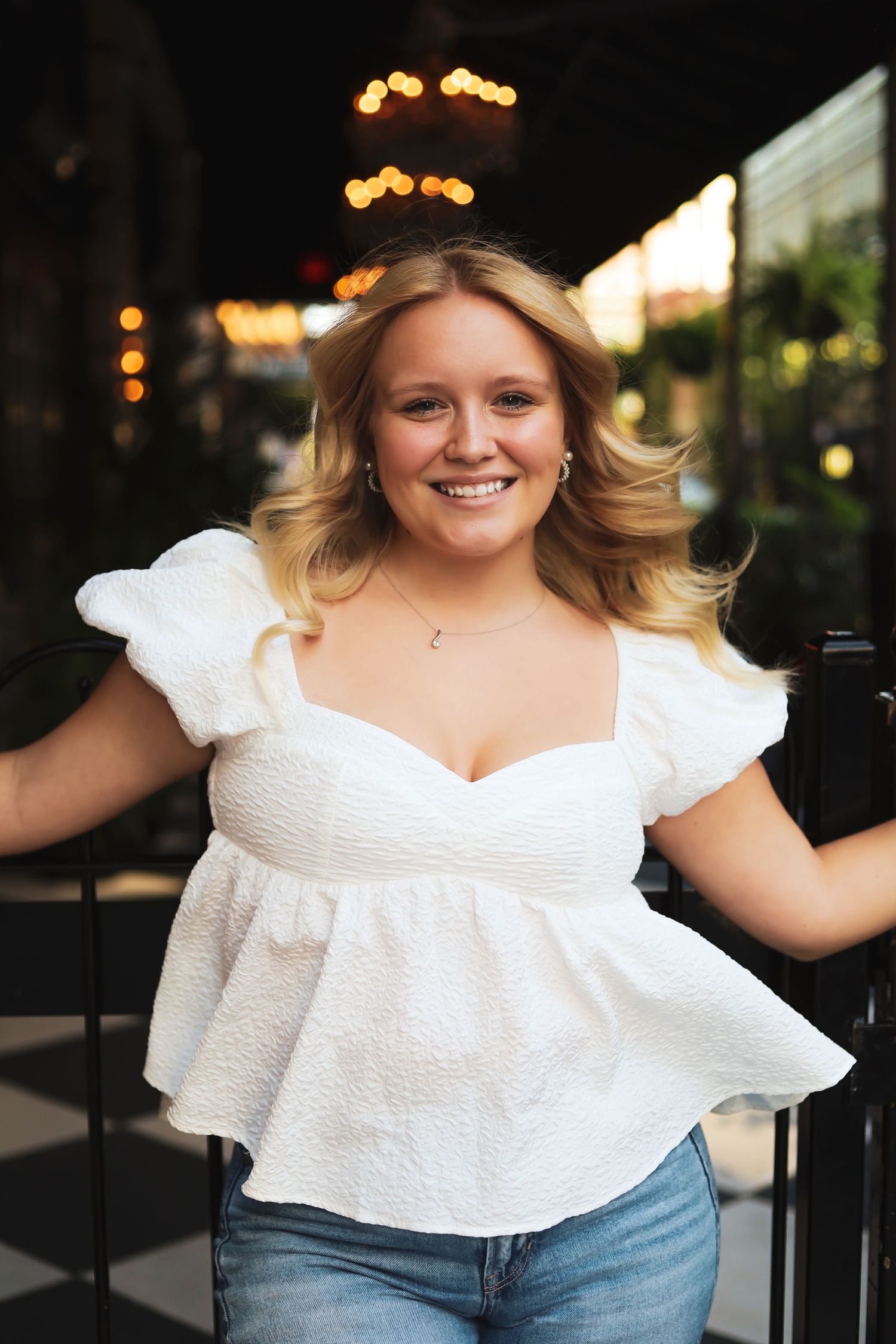 Person in white ruffled top poses against dark background with warm lighting.