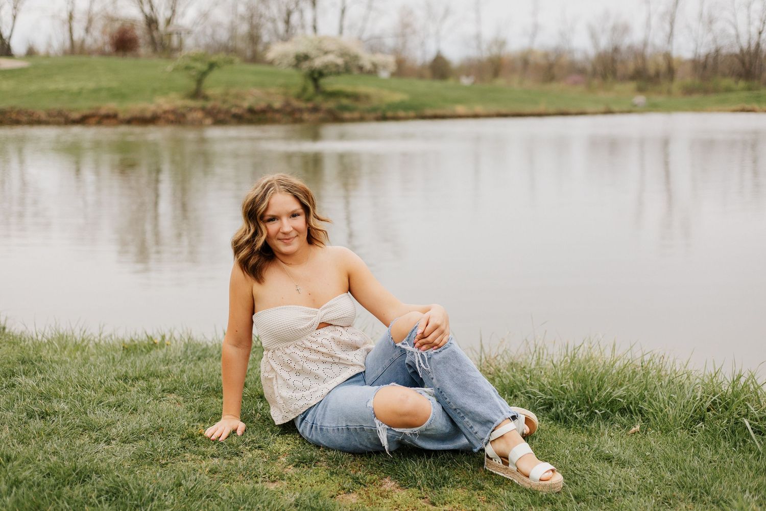 Woman relaxing by a serene pond in casual attire during golden hour.