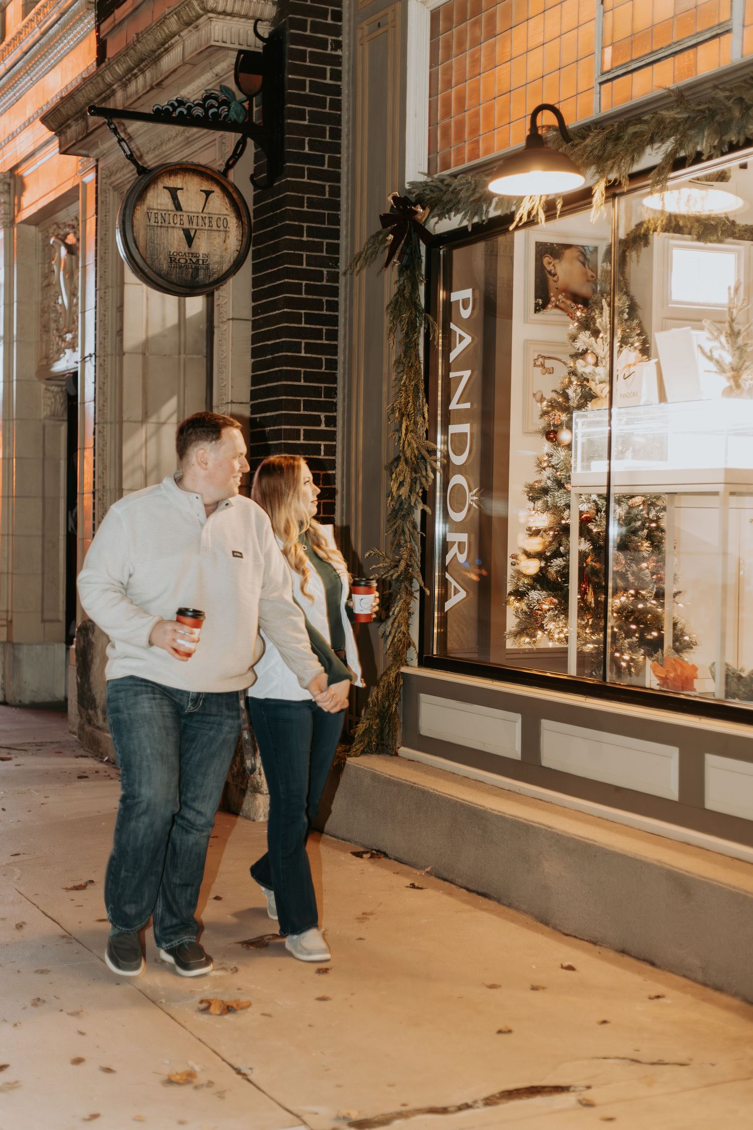 Couple walking past illuminated shop windows with festive holiday decorations.