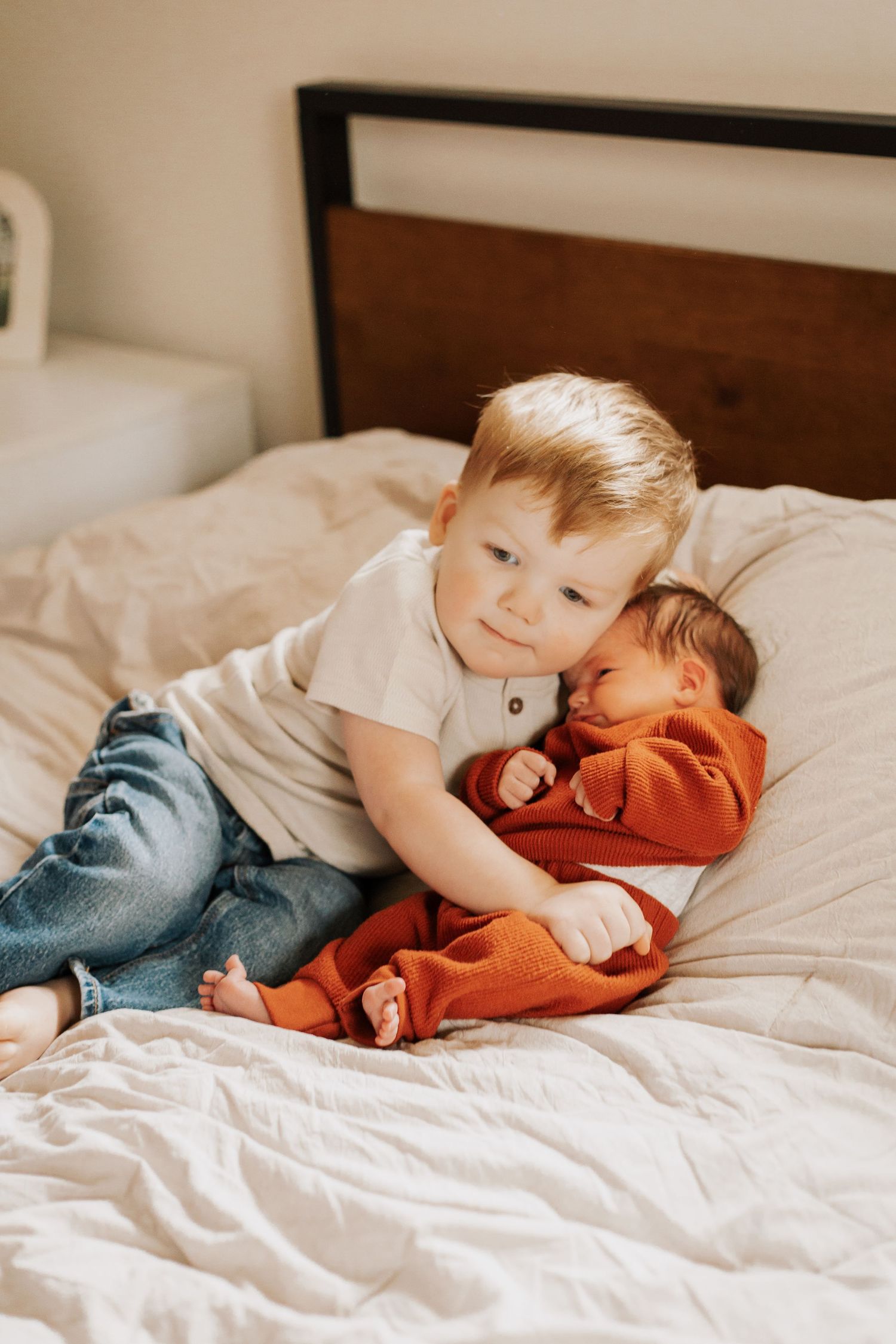 Siblings sharing a tender moment while cuddling on white bedding.
