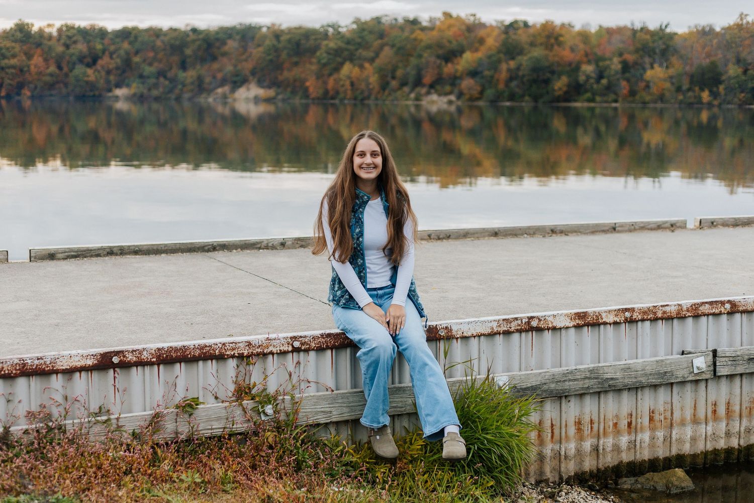 Scenic autumn lakeside view with wooden dock and fall foliage reflecting in calm water.