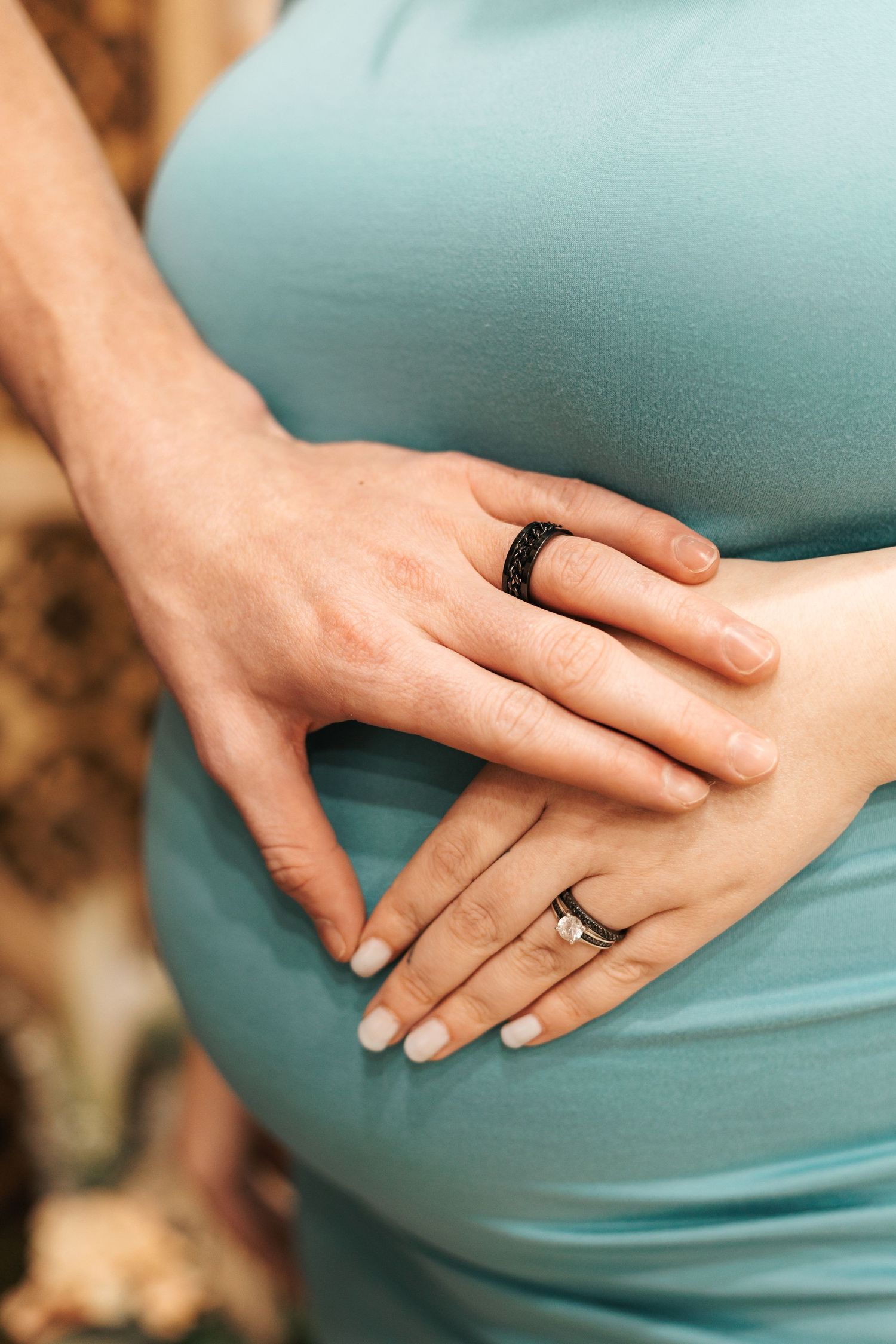 Close-up shots of hands resting on a turquoise maternity dress showing an engagement ring.