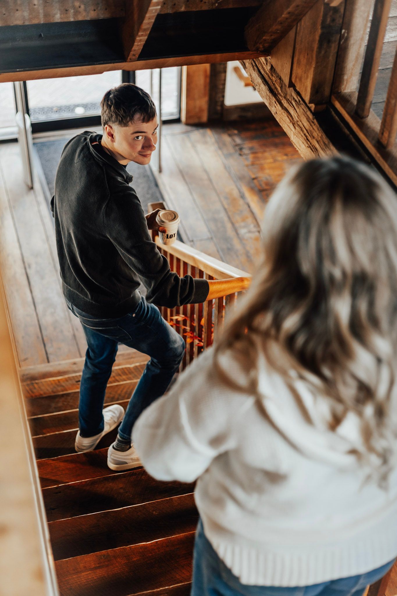 Two people walking up rustic wooden stairs while holding coffee cups.