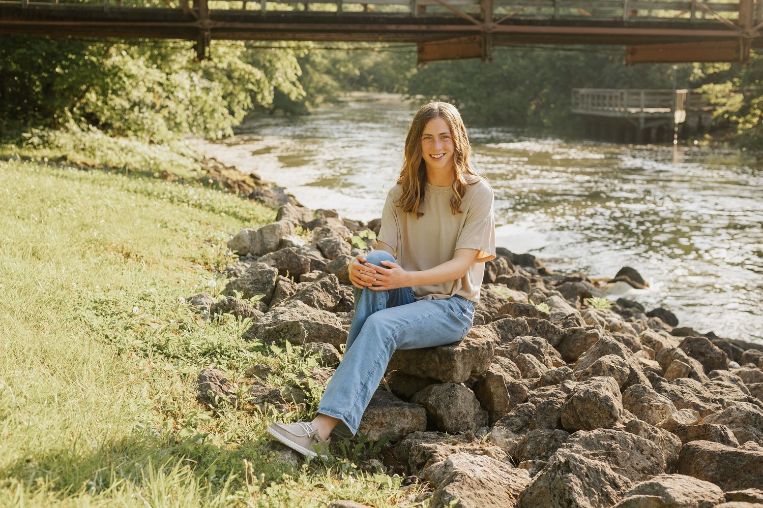 Scenic outdoor photography session by a rocky stream bank in warm sunlight.