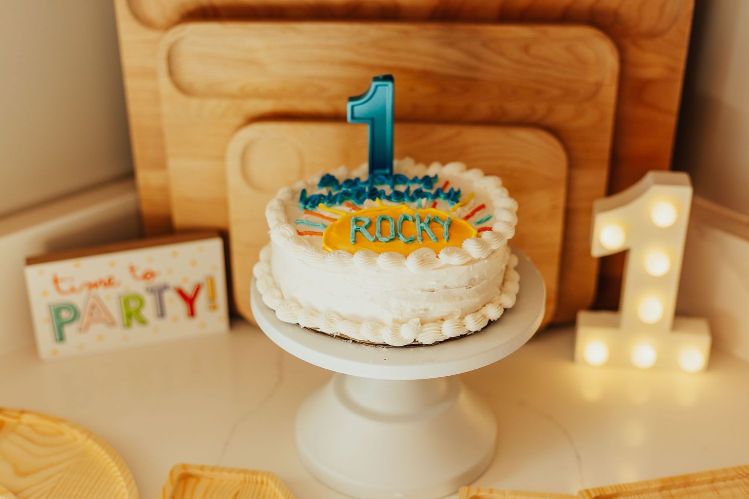 Blue and white birthday cake with number one candle on white table.