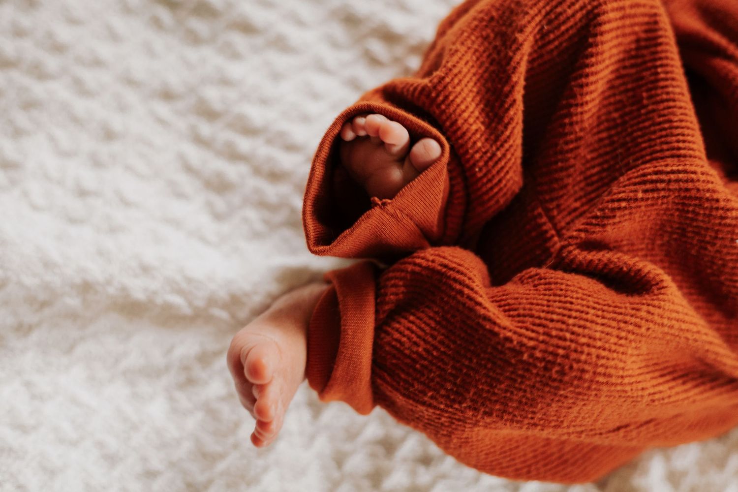 Close-up details of a rust-colored knit blanket with soft texture and folds.