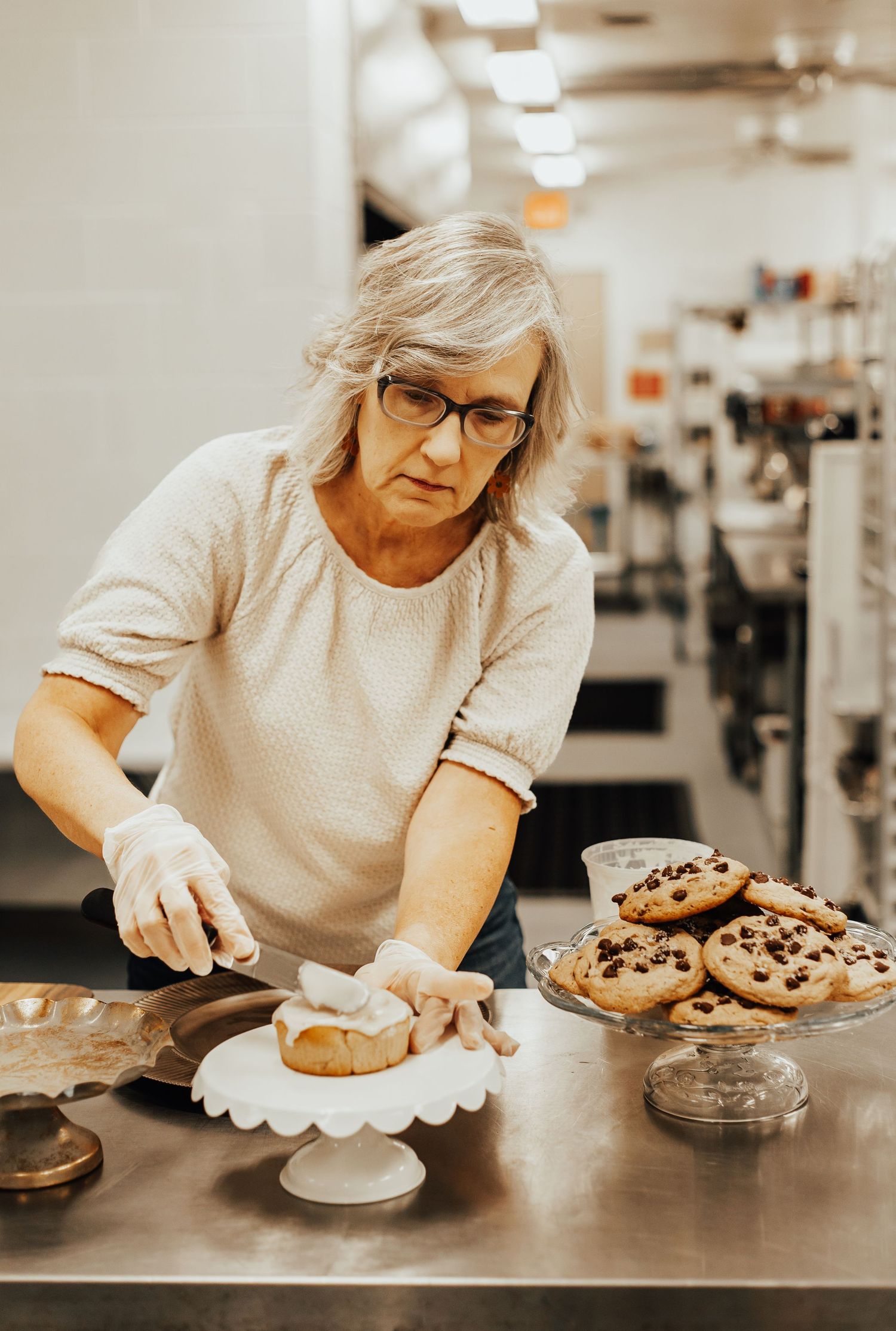 Baker in a white shirt carefully decorating and plating freshly baked desserts in a commercial kitchen.