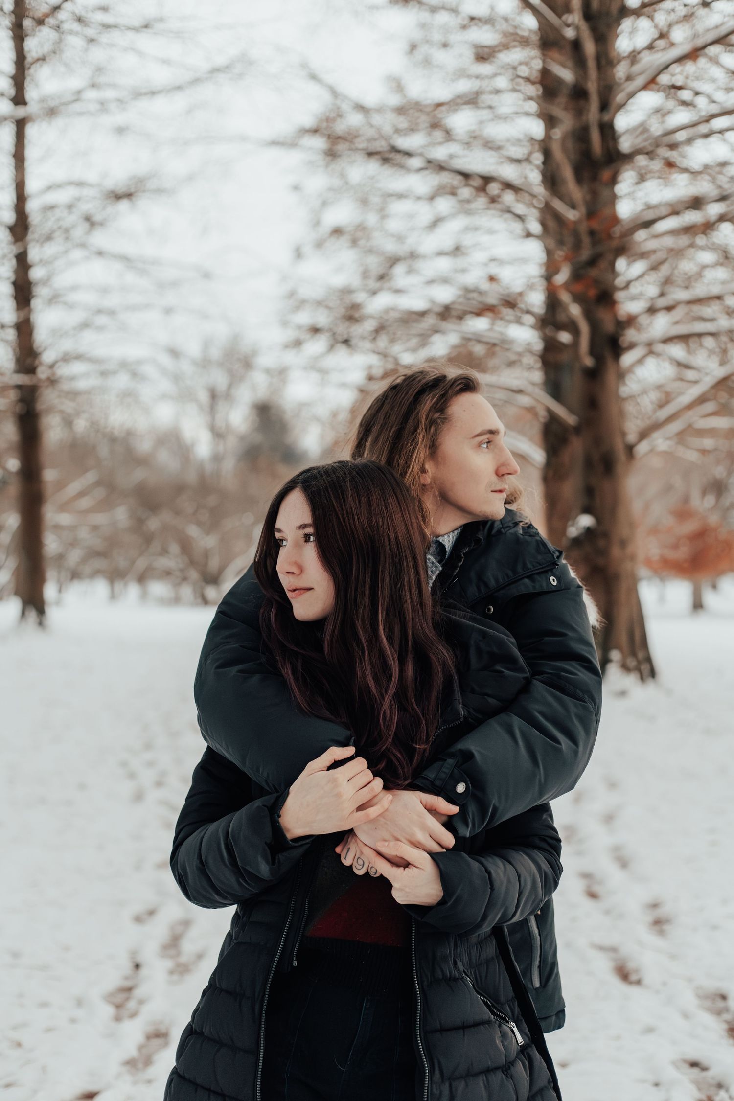 A couple shares an intimate embrace while standing in a winter forest landscape.