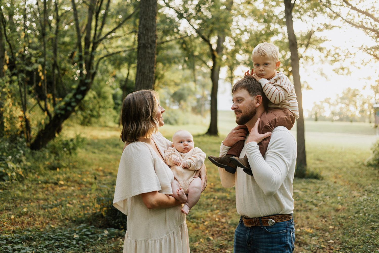 Family gathering outdoors in a park during golden hour with trees in the background.