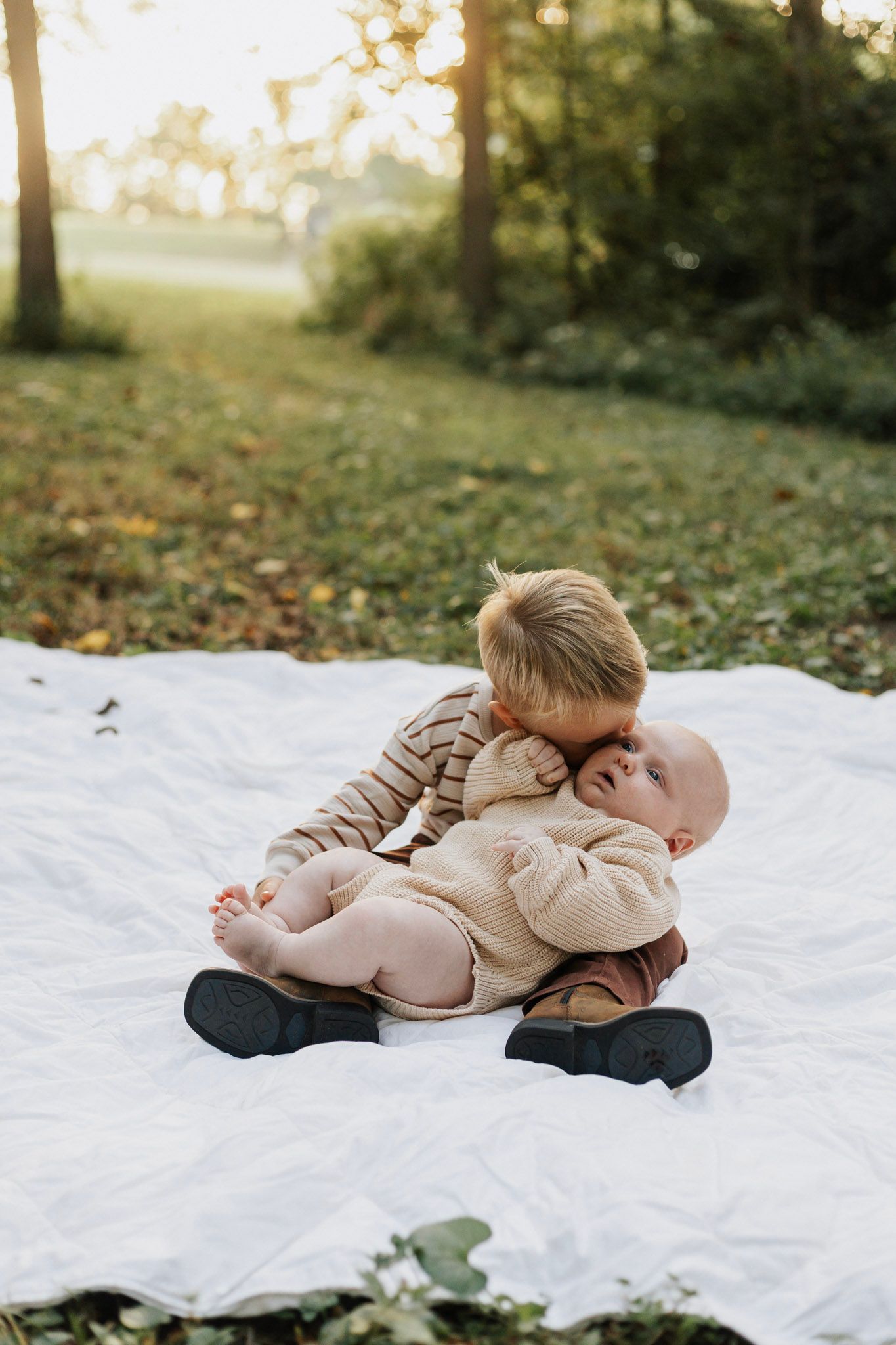 Two children playing together on a white blanket outdoors.