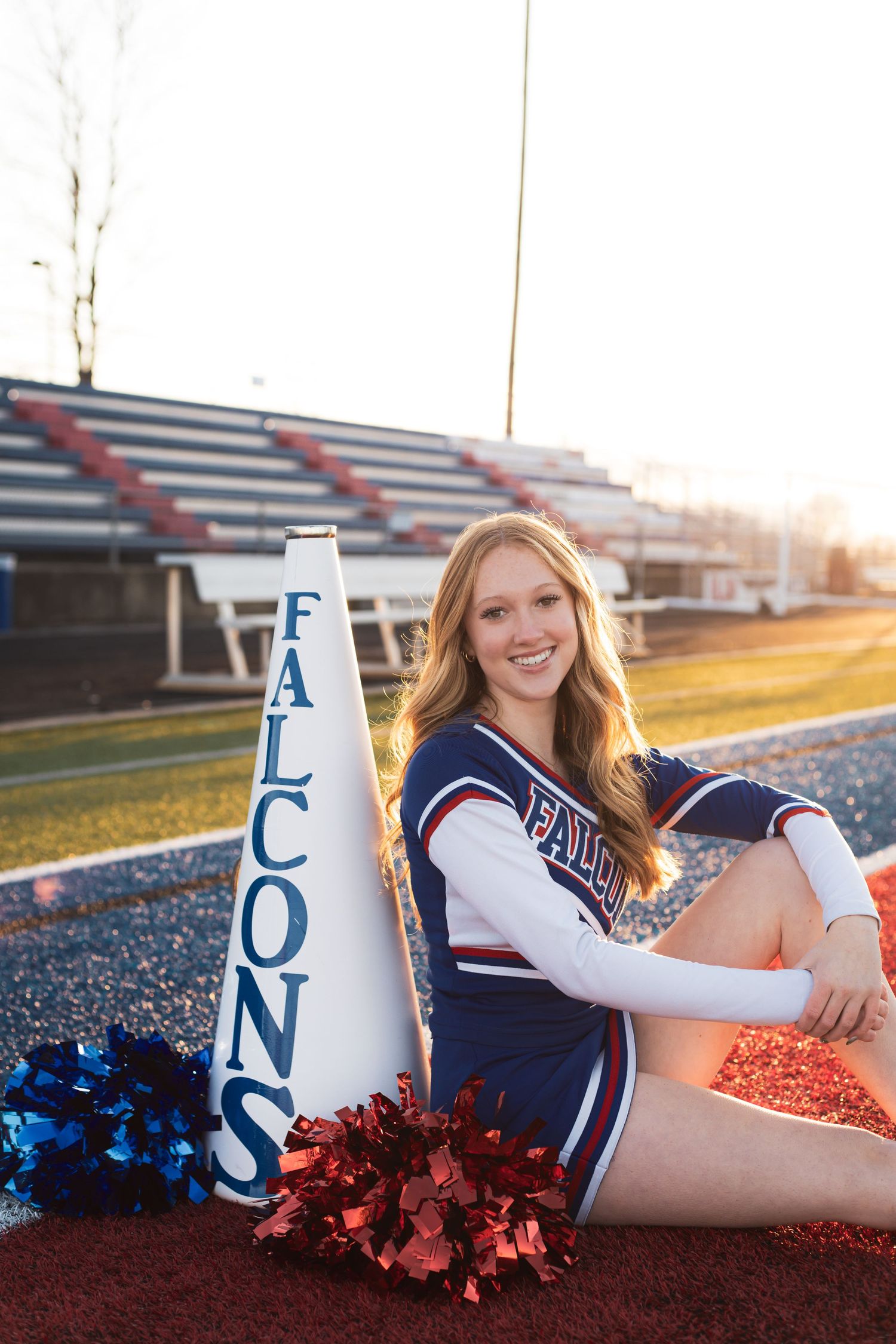 Cheerleader portrait on sports field with megaphones and pom poms at sunset.