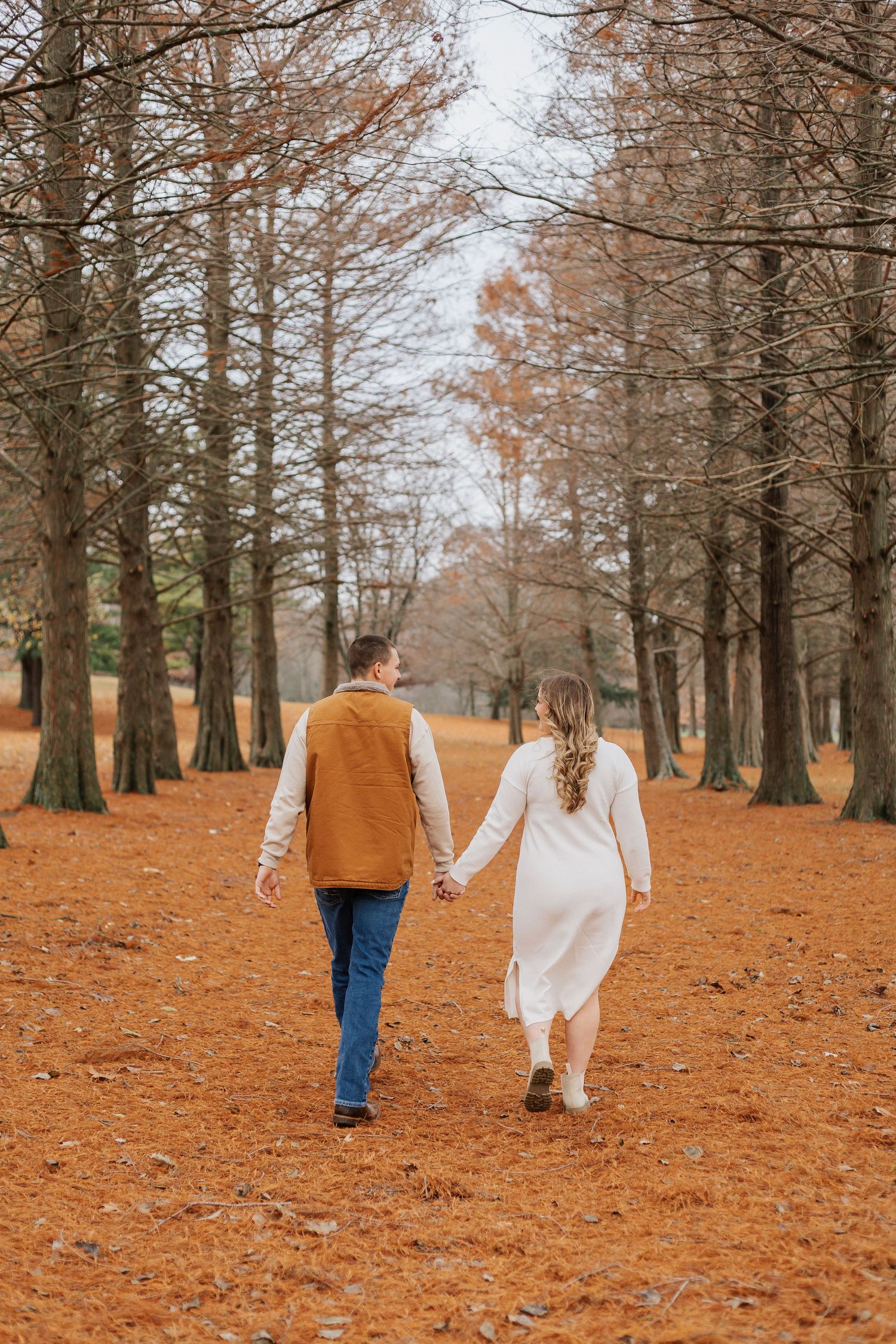 Couple walking through a forest path covered in fallen orange autumn leaves.