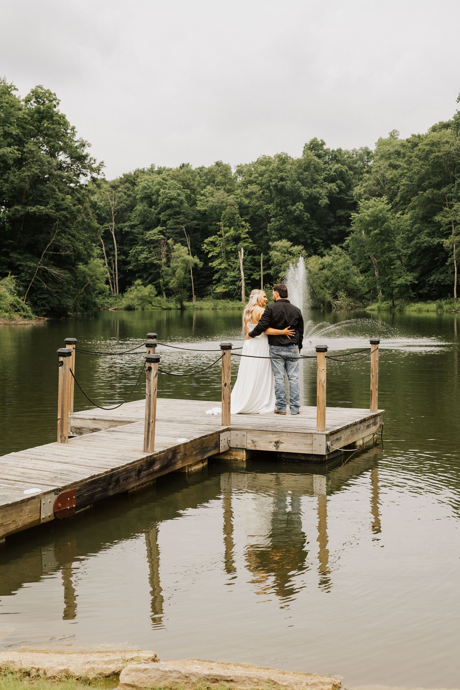 A wooden dock extends over a serene lake surrounded by lush green trees on a summer day.