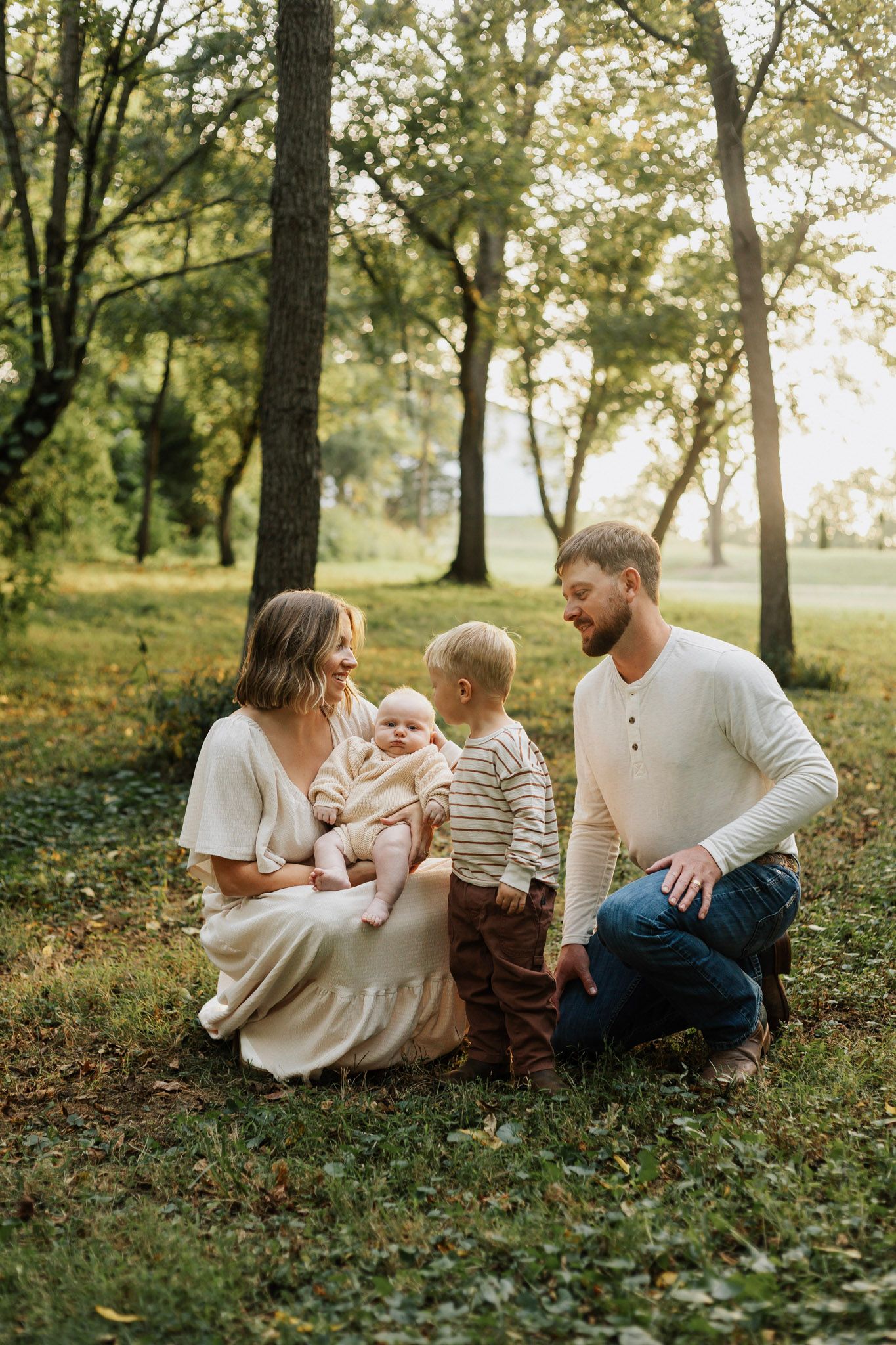 Family relaxing together on grass under trees during a warm afternoon.