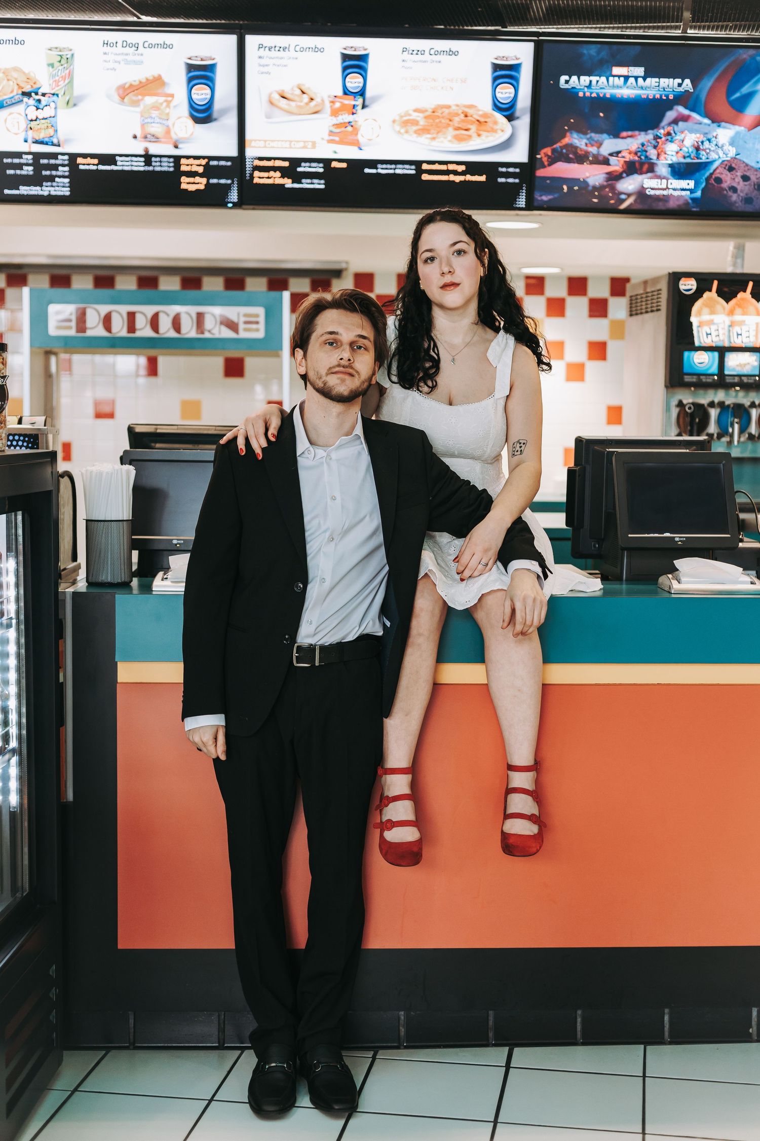 Playful couple posing at a retro-style fast food counter with orange and teal decor.