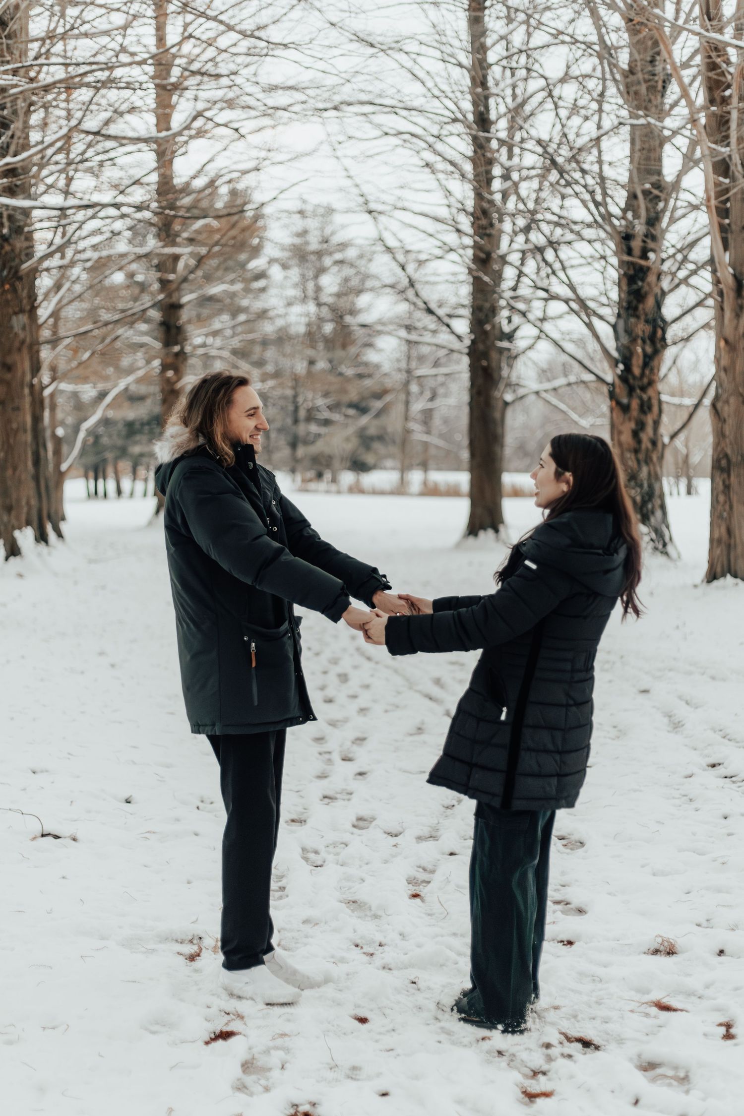 Two people holding hands in a snowy winter forest setting.