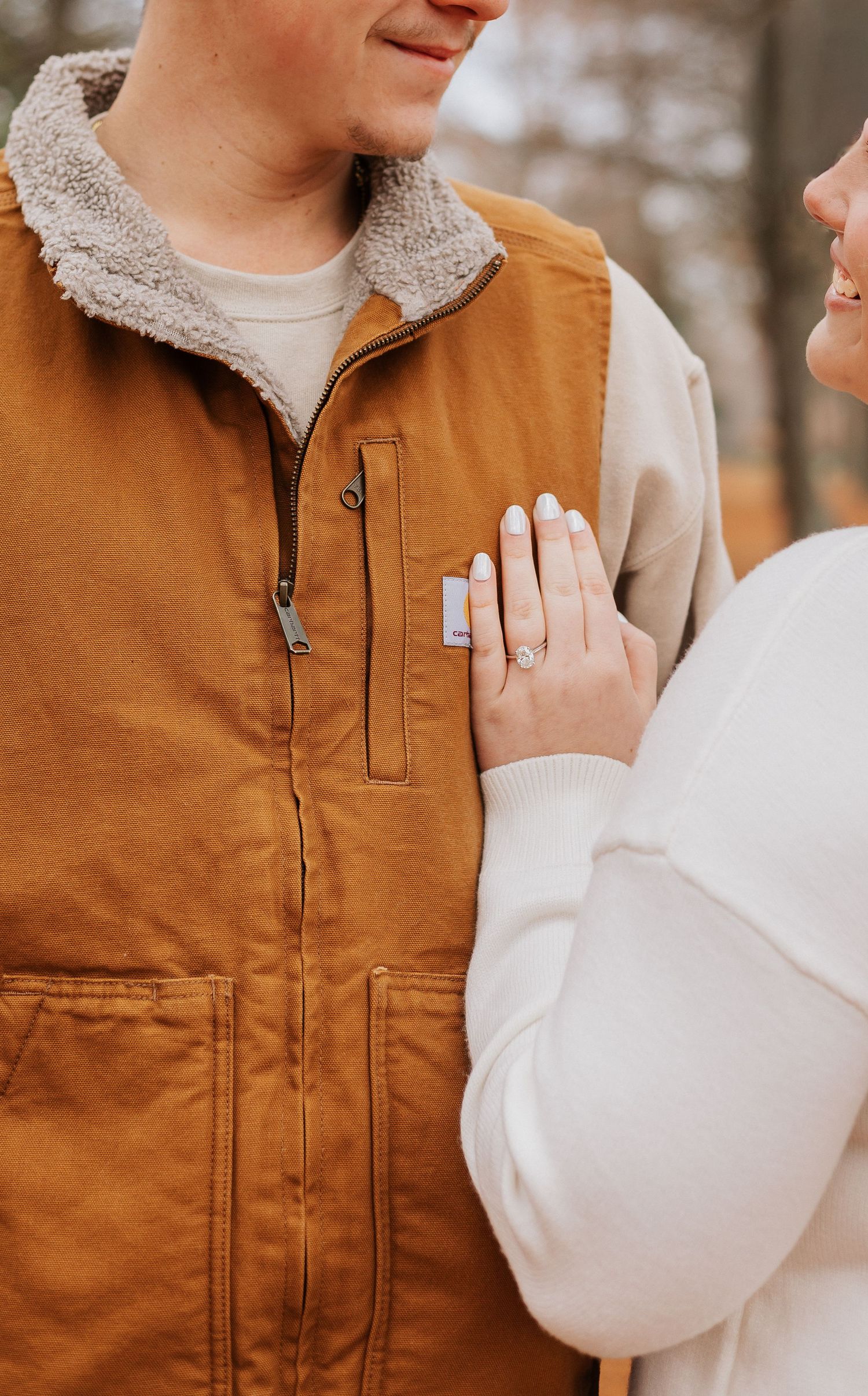 Close-up details of a brown Carhartt vest and white sweater against an autumn backdrop.