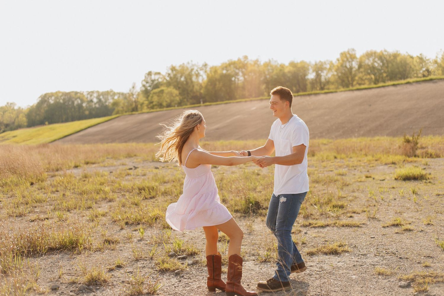 Couple dancing together in an open field during sunset with mountains in background.
