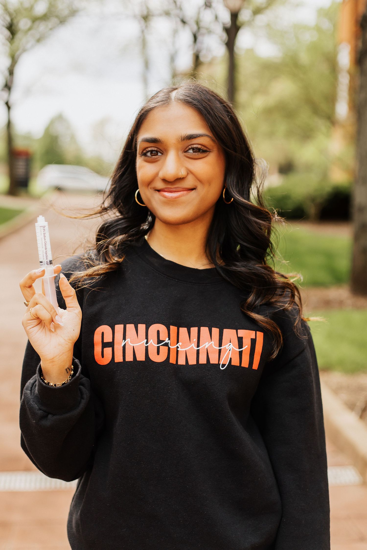 Person wearing black Cincinnati sweatshirt holding up graduation cap outdoors.