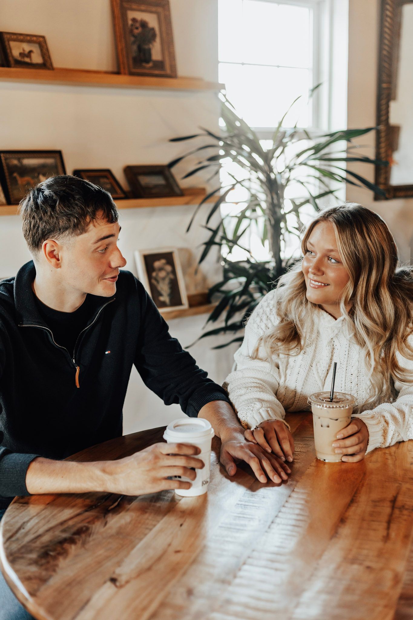 Casual conversation over coffee at wooden table with family photos displayed on wall shelves.