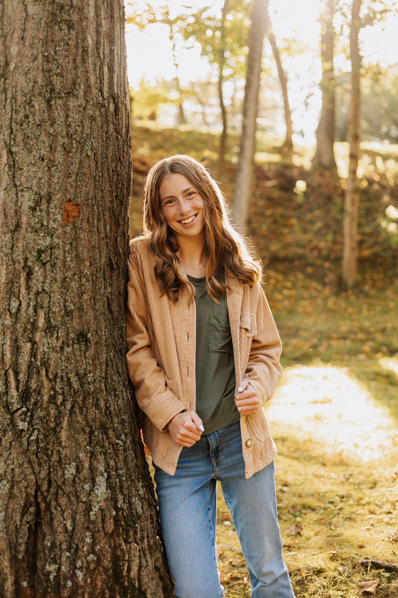 Golden hour portraits between large tree trunks in a sunlit forest setting.