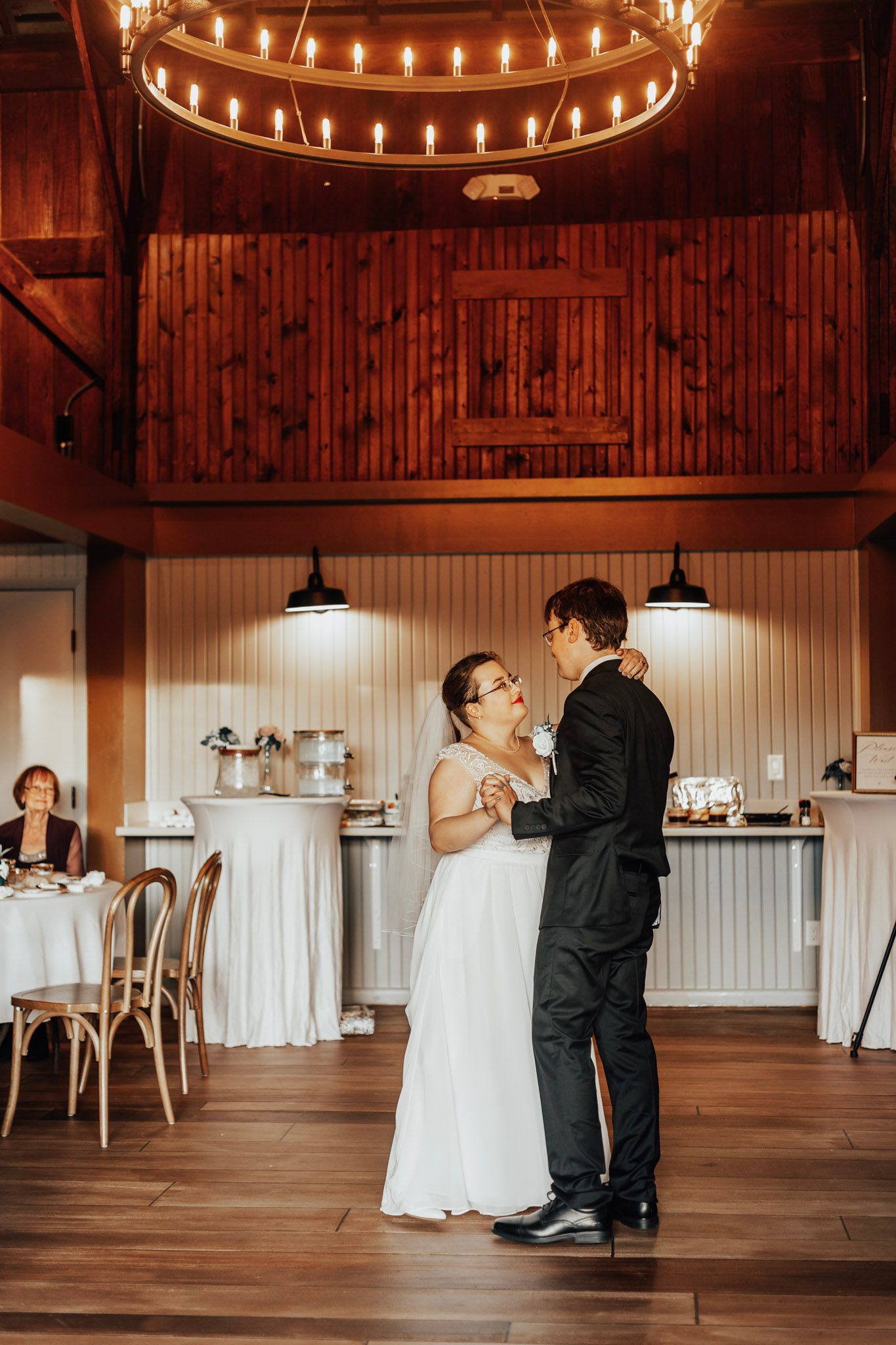 Wedding couple dancing in a rustic venue with string lights overhead and wooden floors.