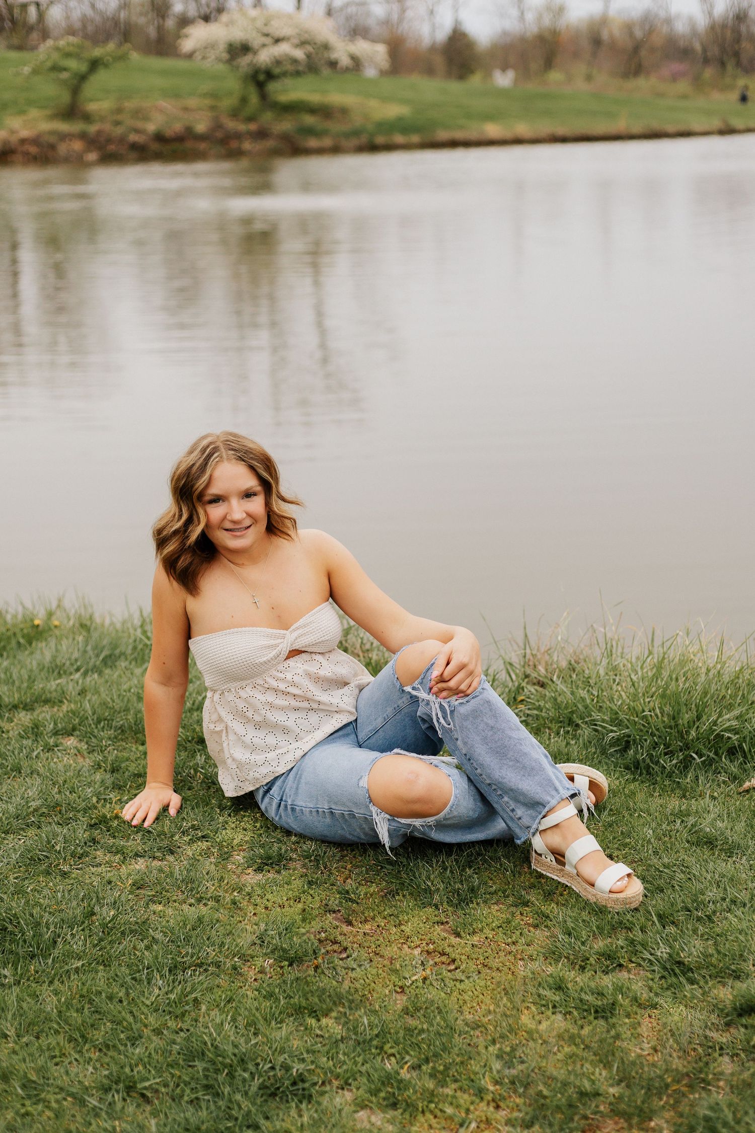 Casual outdoor portrait by lake wearing distressed jeans and cream top.