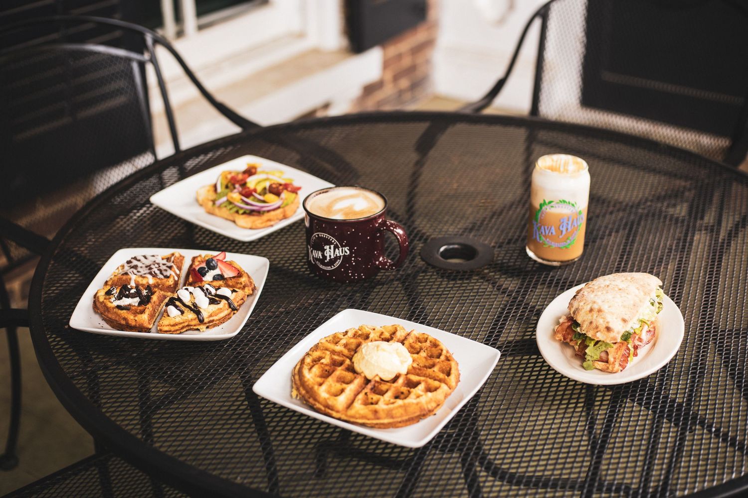 Outdoor table setting with waffles and breakfast plates on a metal patio table.