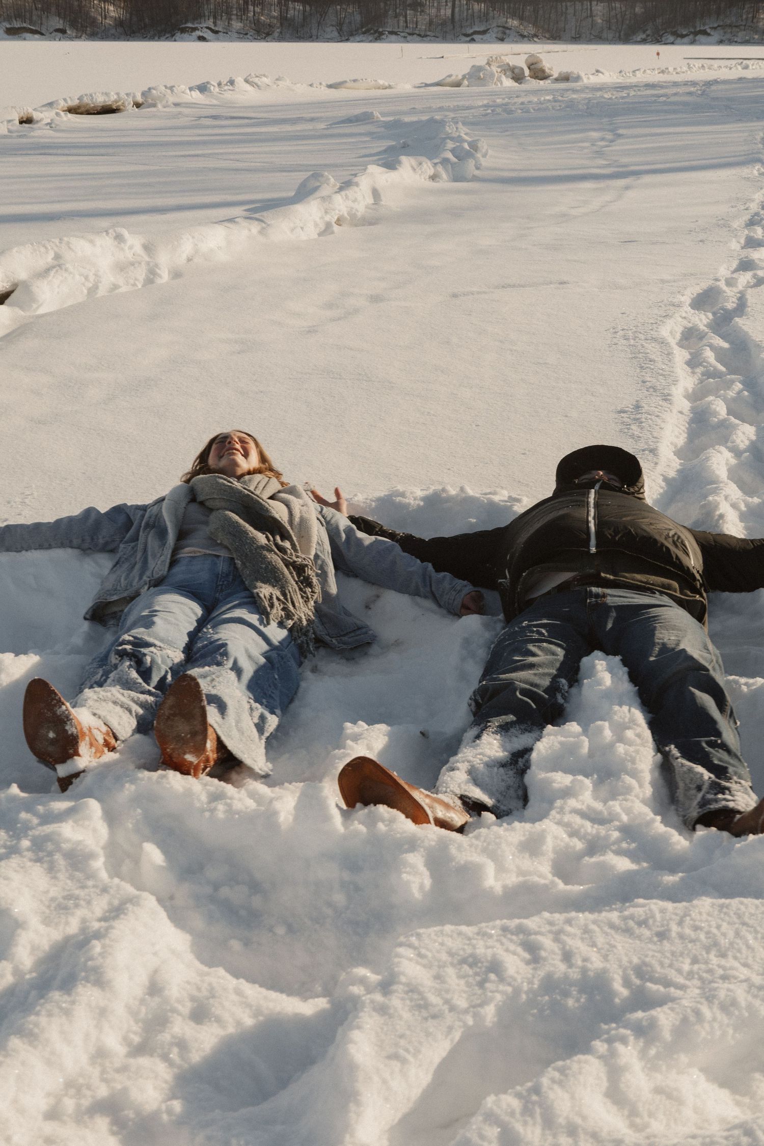 Two people lying in fresh snow during a winter photo session.