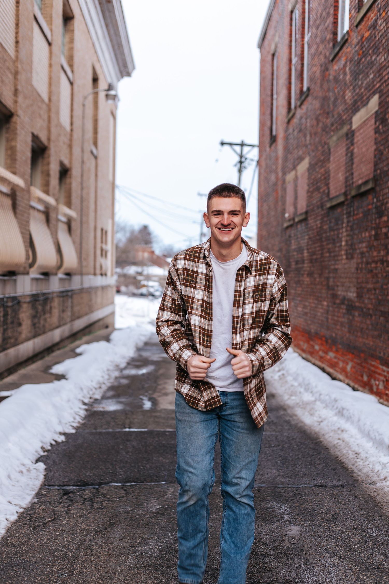 Casual portrait of a person in plaid flannel shirt standing between brick buildings in winter.