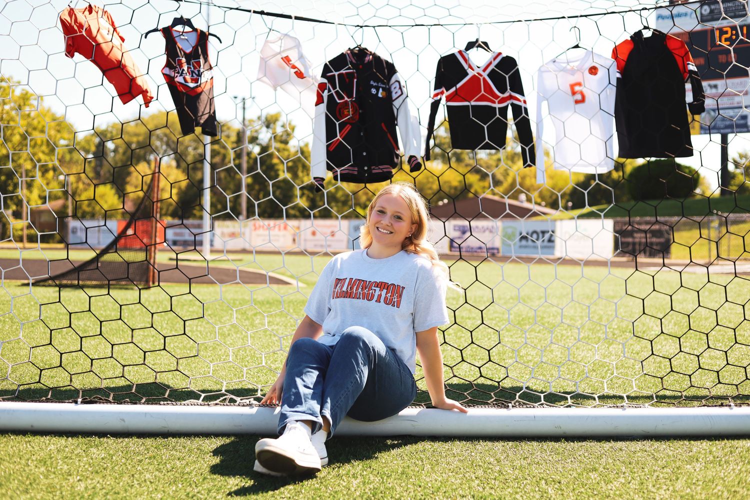 Person in athletic wear stretching near soccer goal on sunny sports field.
