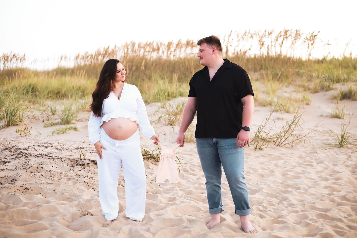 Couple walking together on sandy beach during maternity photoshoot.