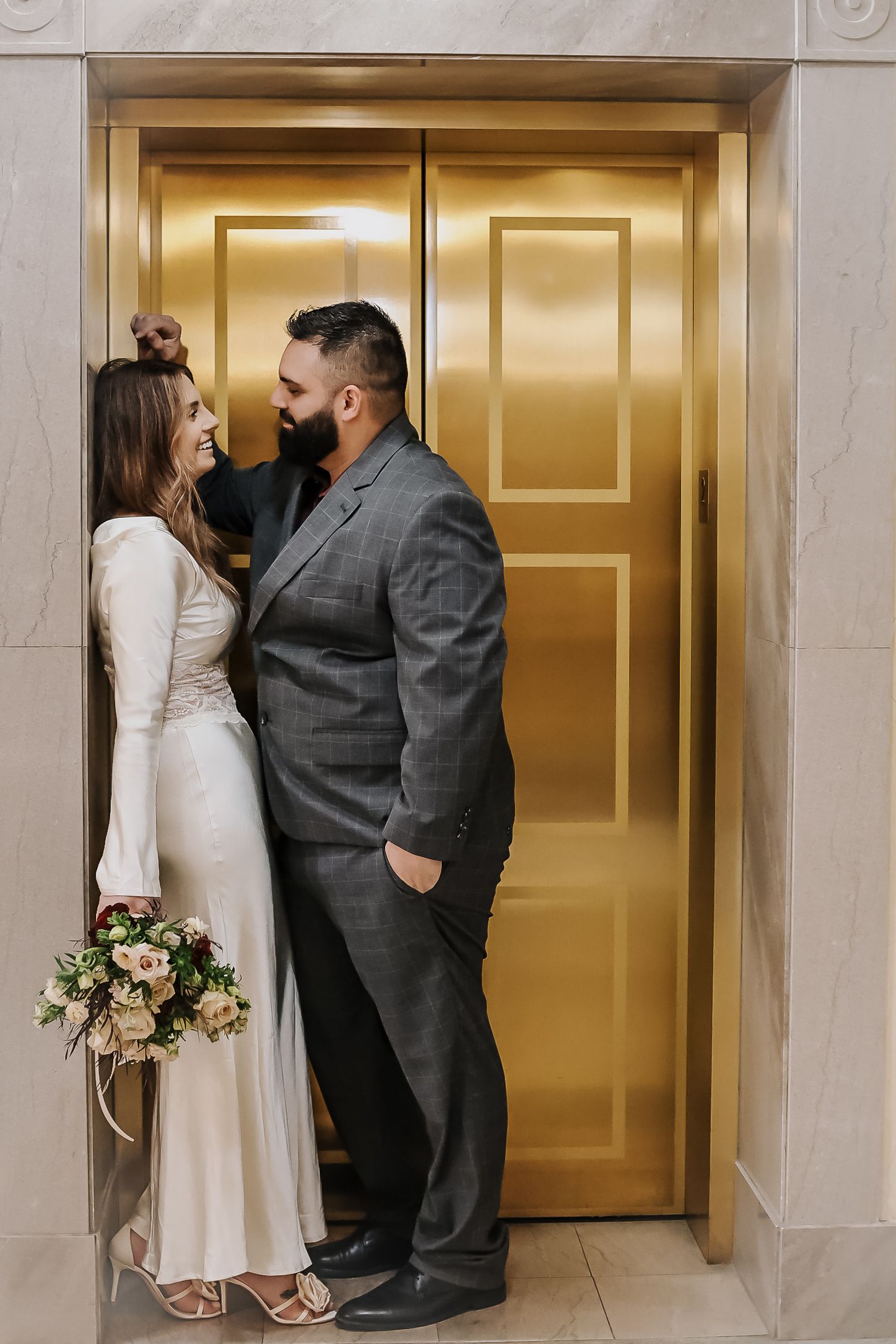 Wedding couple sharing intimate moments by golden elevator doors.