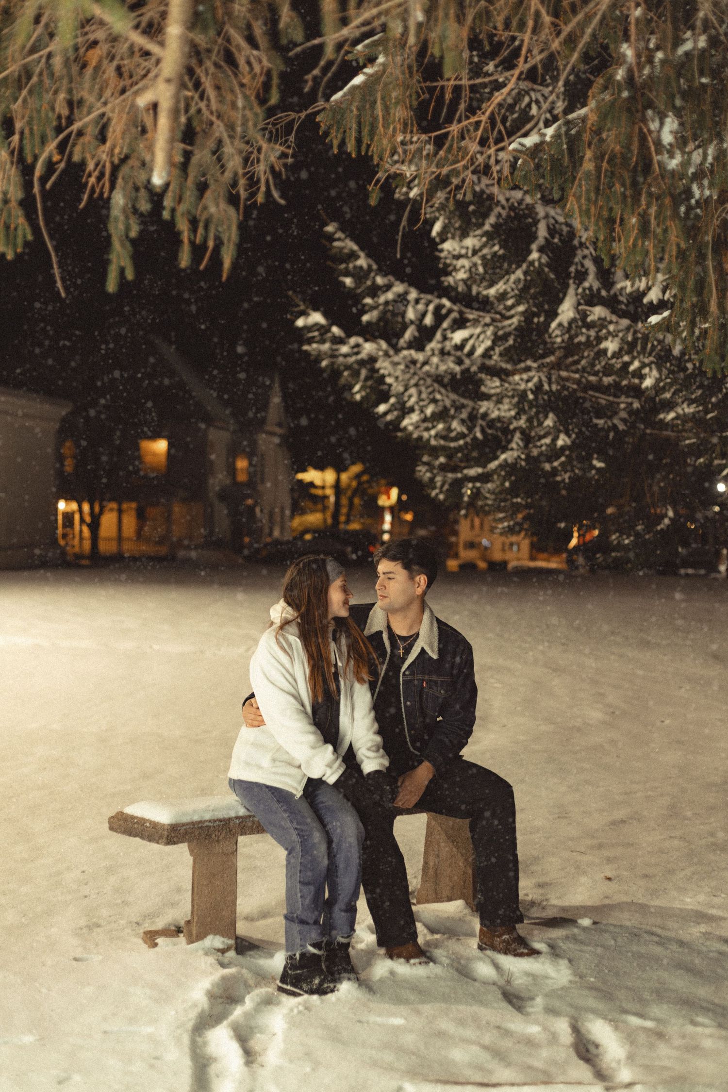 Two people playing in the snow at night with snow-covered trees in the background.