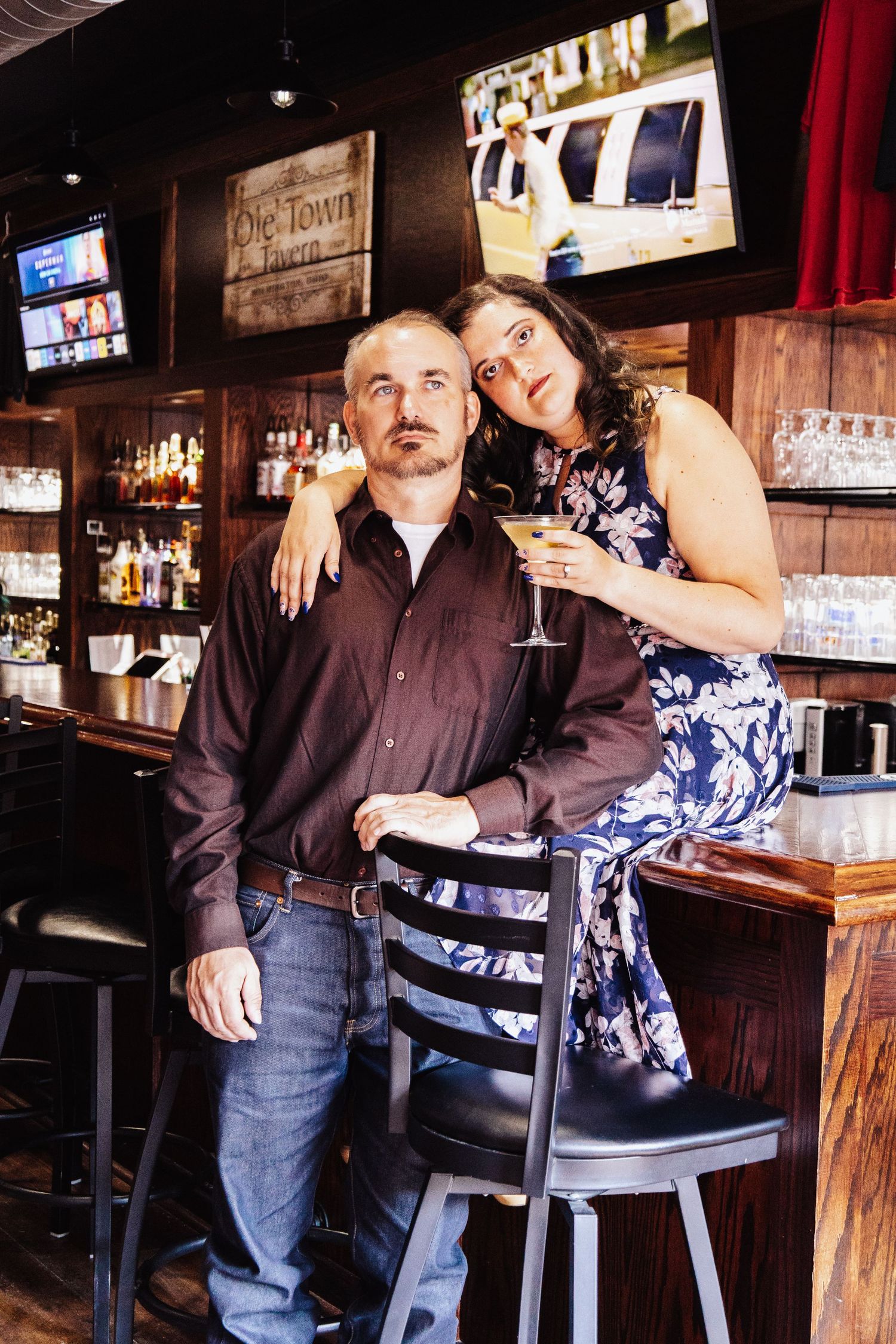 Couple poses casually at a bar counter with rustic decor and ambient lighting.